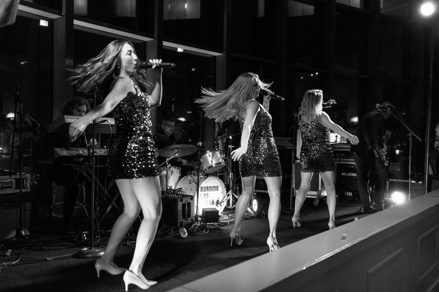 Female performers in sequined dresses singing on stage with a band.