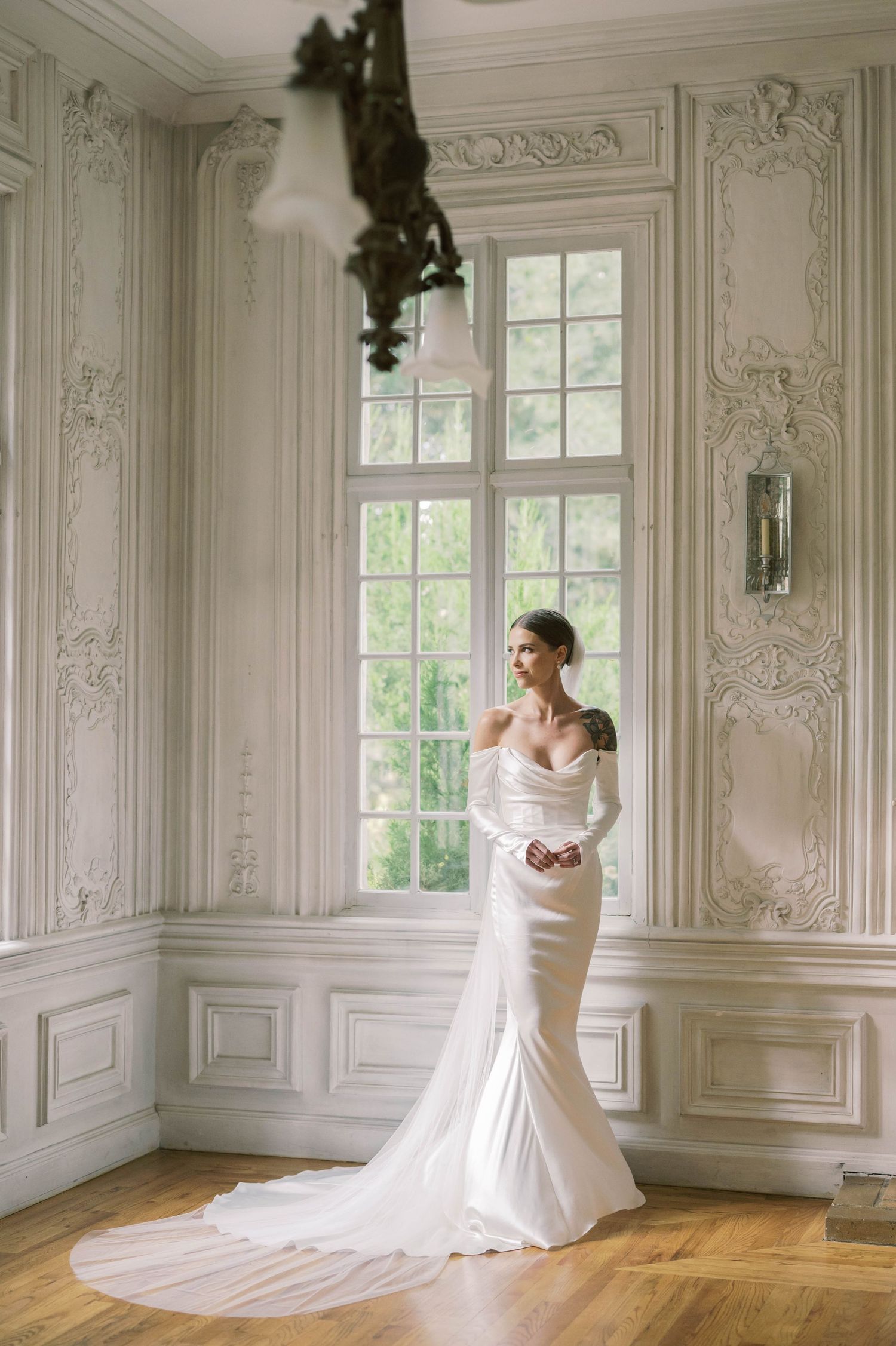 Elegant white mermaid wedding dress photographed in a bright French-style room with ornate moldings.