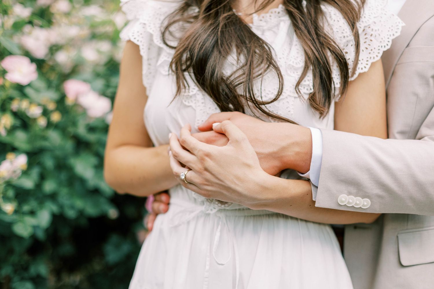 Close up of hands embracing with lace dress details and light suit jacket visible.