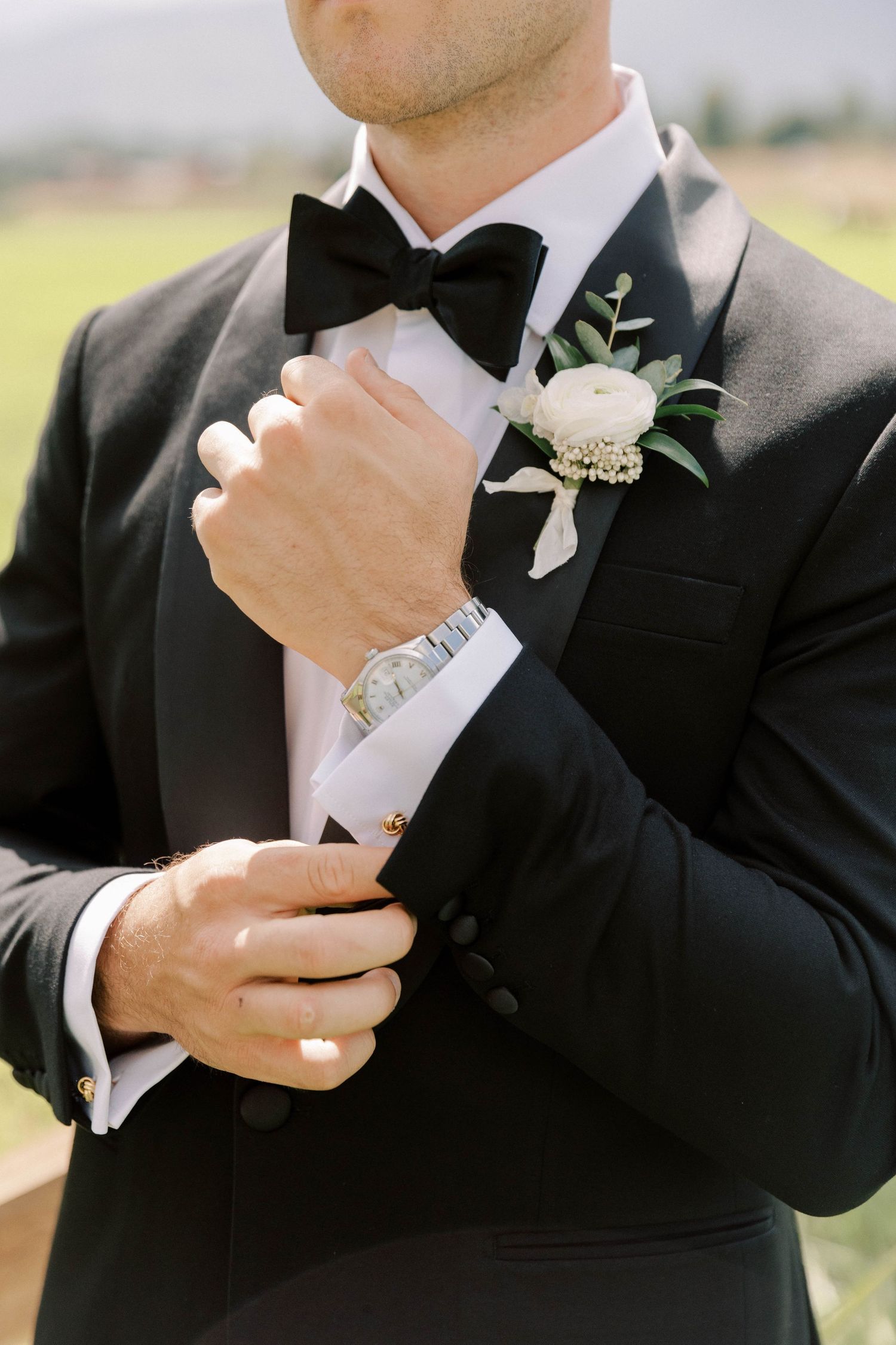 Close-up of groom adjusting his bowtie with white floral boutonniere.
