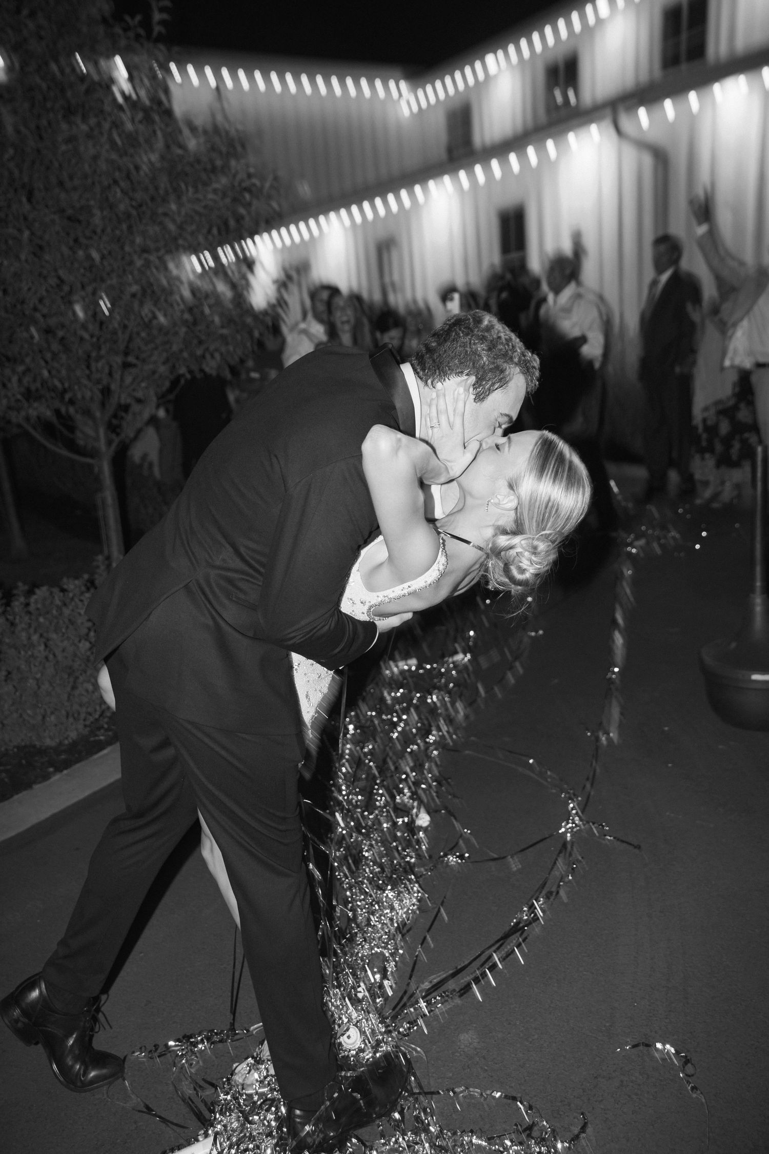 A romantic dip kiss during an evening celebration with string lights overhead.
