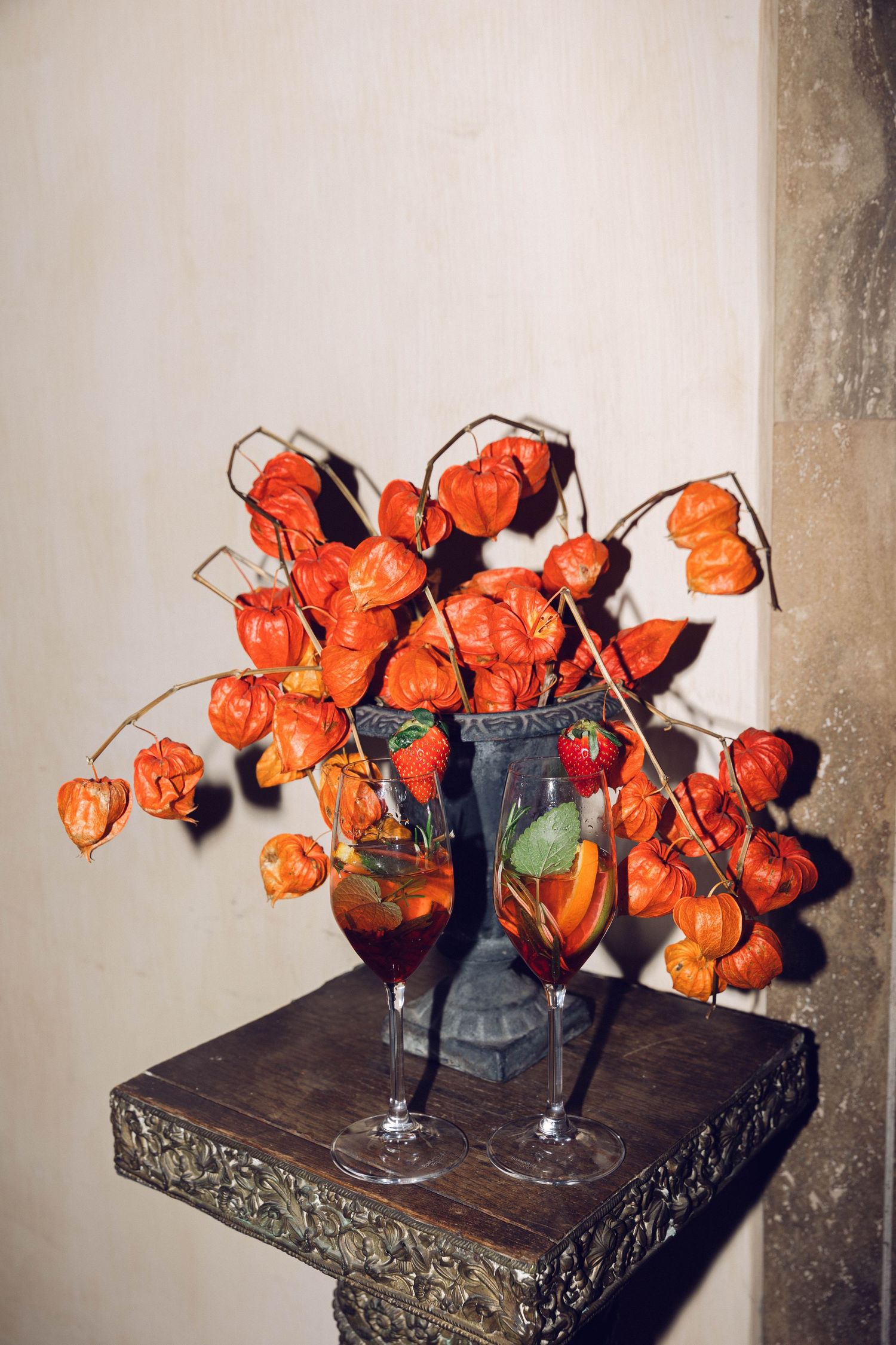 Chinese lantern flowers arranged in wine glasses on dark wooden table.
