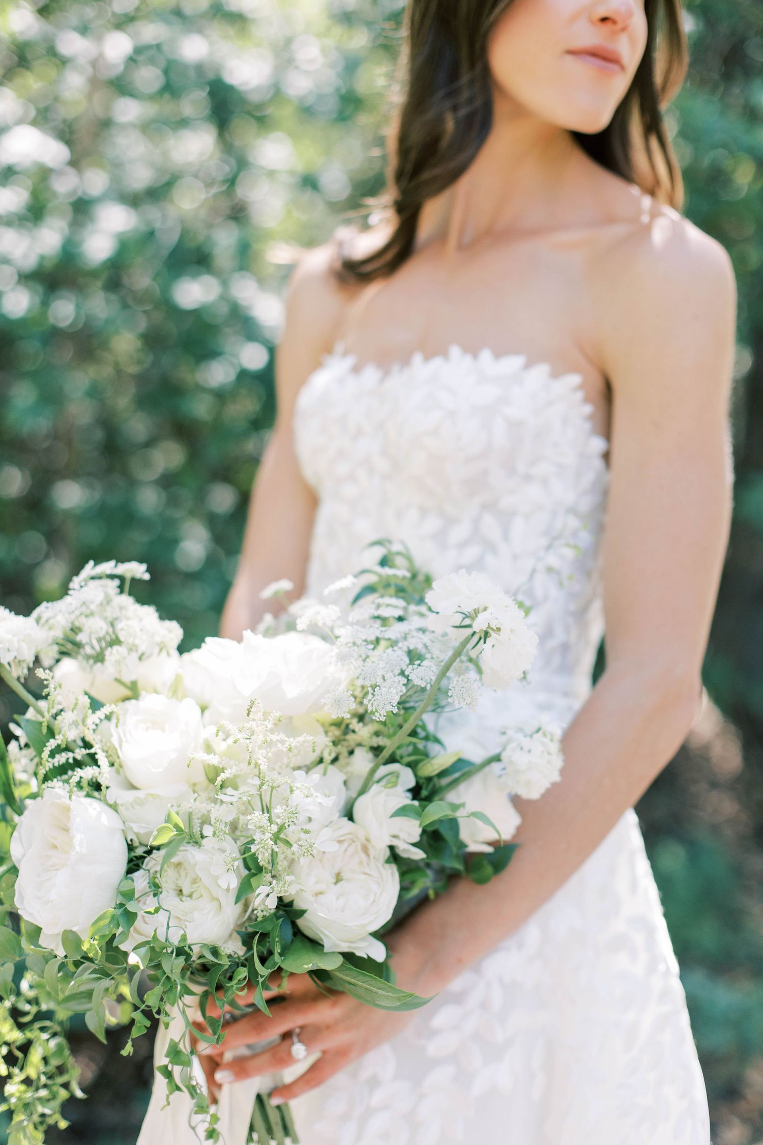 Bride holding elegant white and green wedding bouquet against natural outdoor backdrop.
