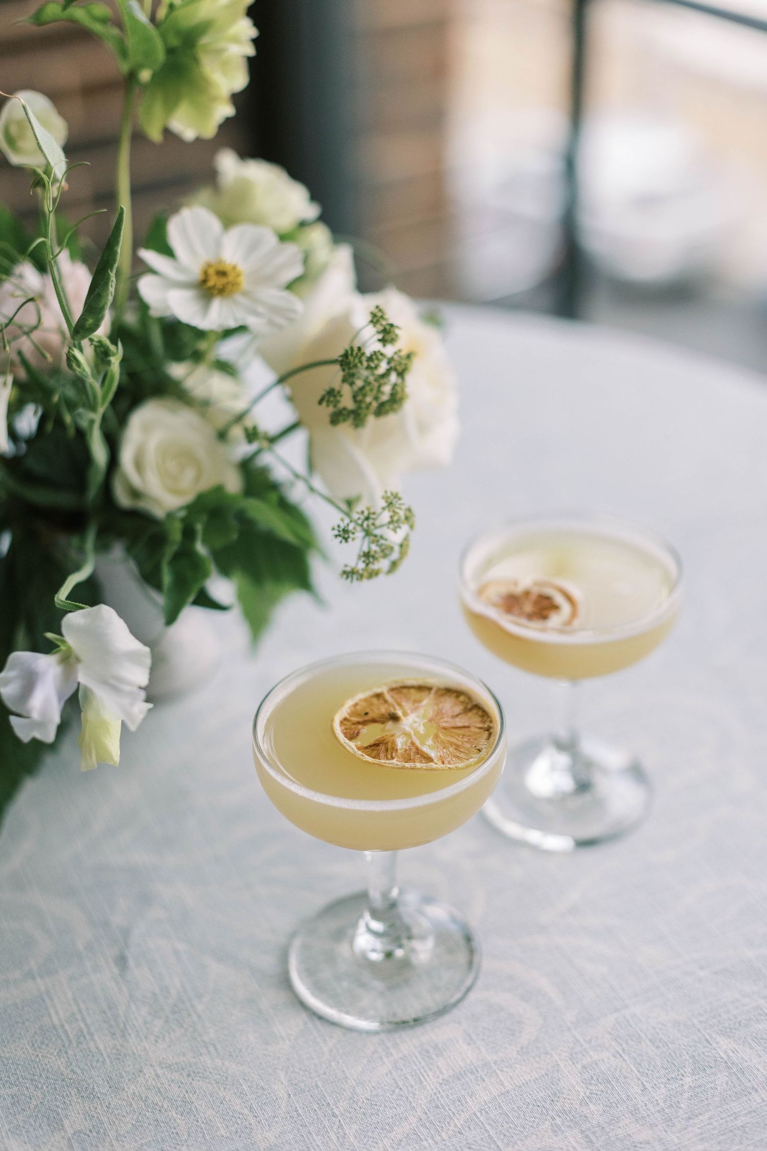 Citrus cocktails garnished with dried lemon slices beside white floral arrangements.