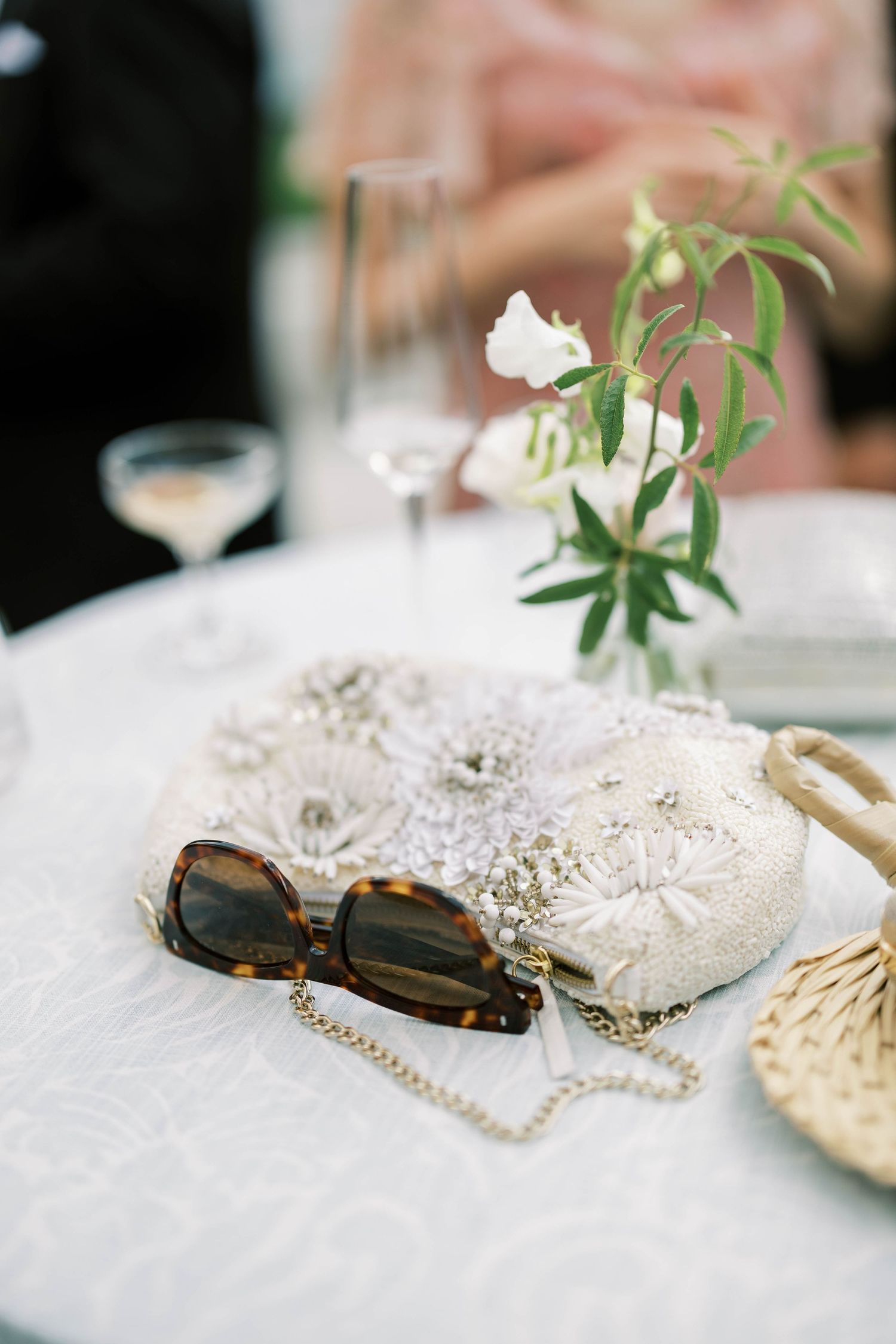 Wedding accessories including sunglasses and lace clutch with delicate floral centerpiece.