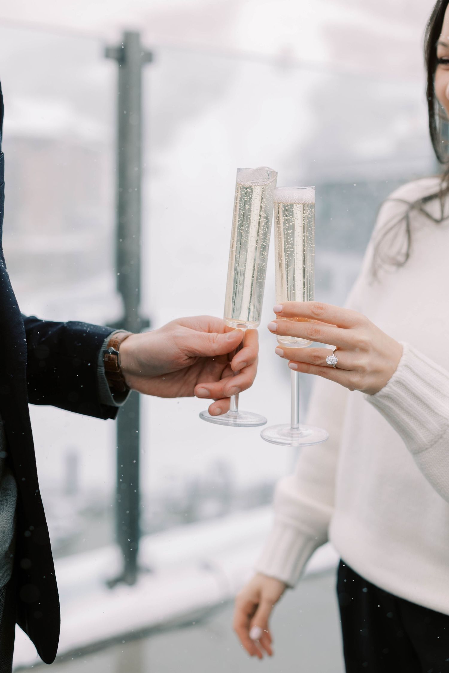 Two hands holding champagne flutes on a snowy rooftop terrace during a celebration at the pendry park city.