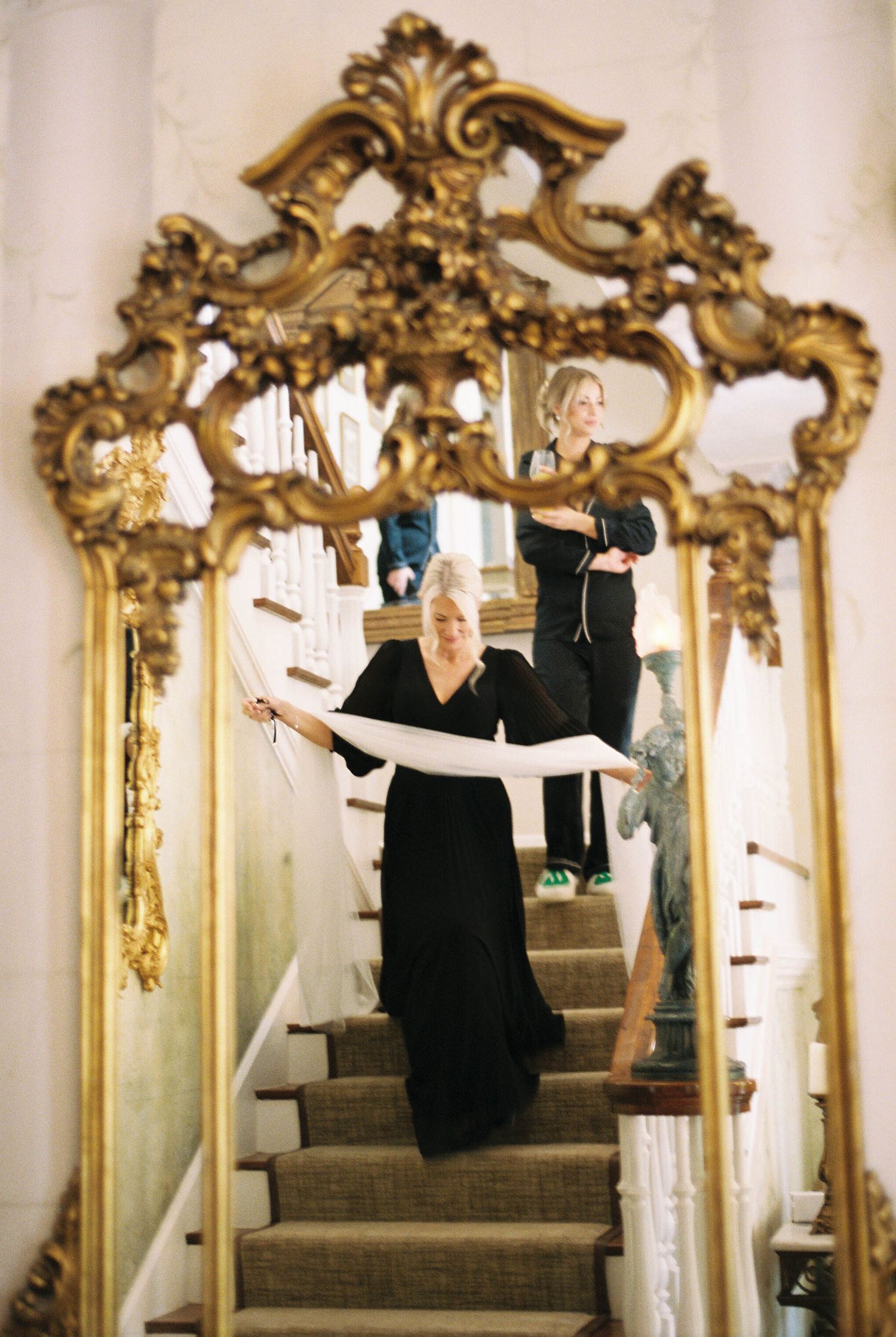 Ornate gold mirror frames figure in black dress striking dance pose on staircase.