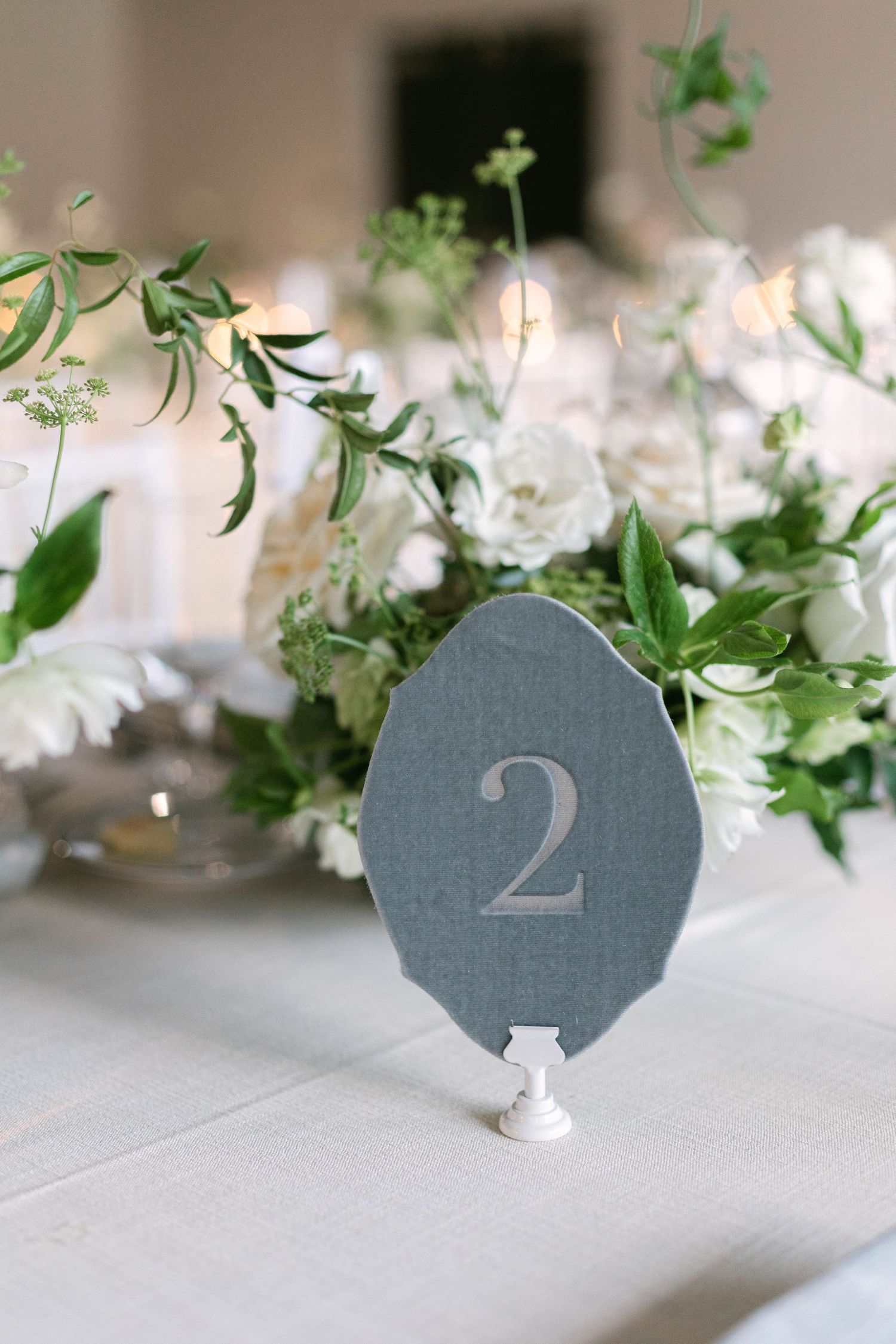 Gray table number two card surrounded by white flowers and greenery at wedding reception.