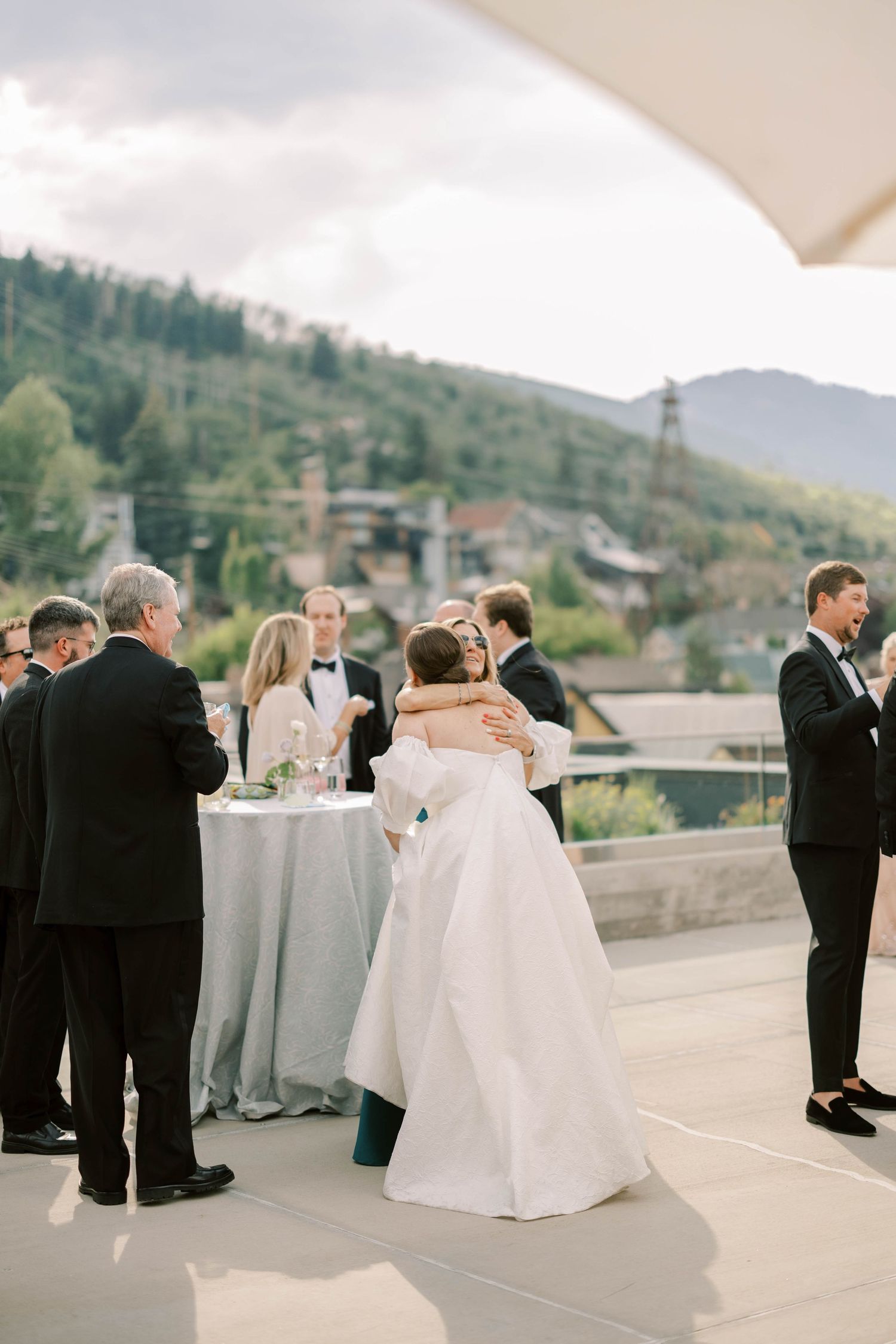 Wedding guests socializing on an outdoor terrace with mountain views in the background.