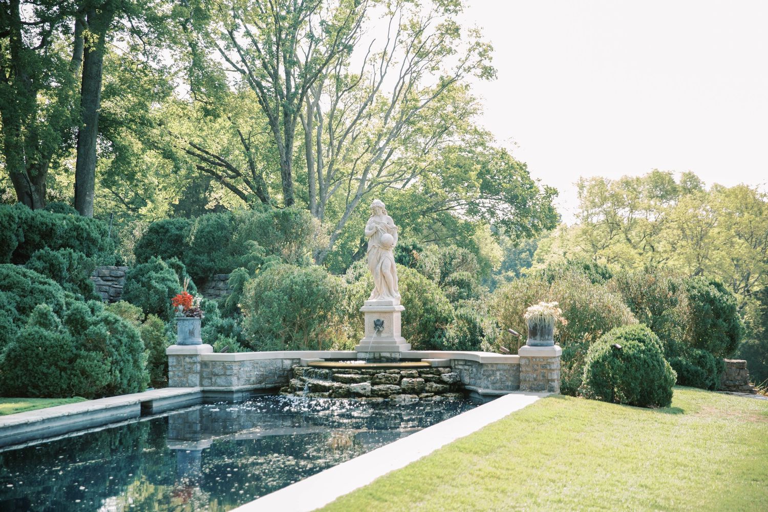 Classical garden pool with stone statues and manicured hedges in elegant landscape design in Cheekwood.