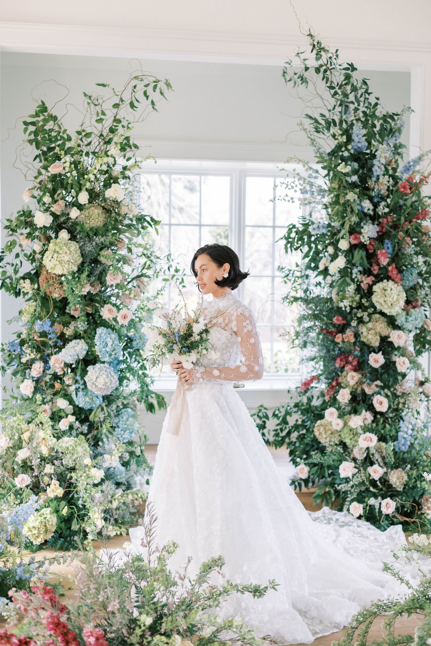 A wedding dress showcased between two towering floral arrangements with greenery and white blooms.
