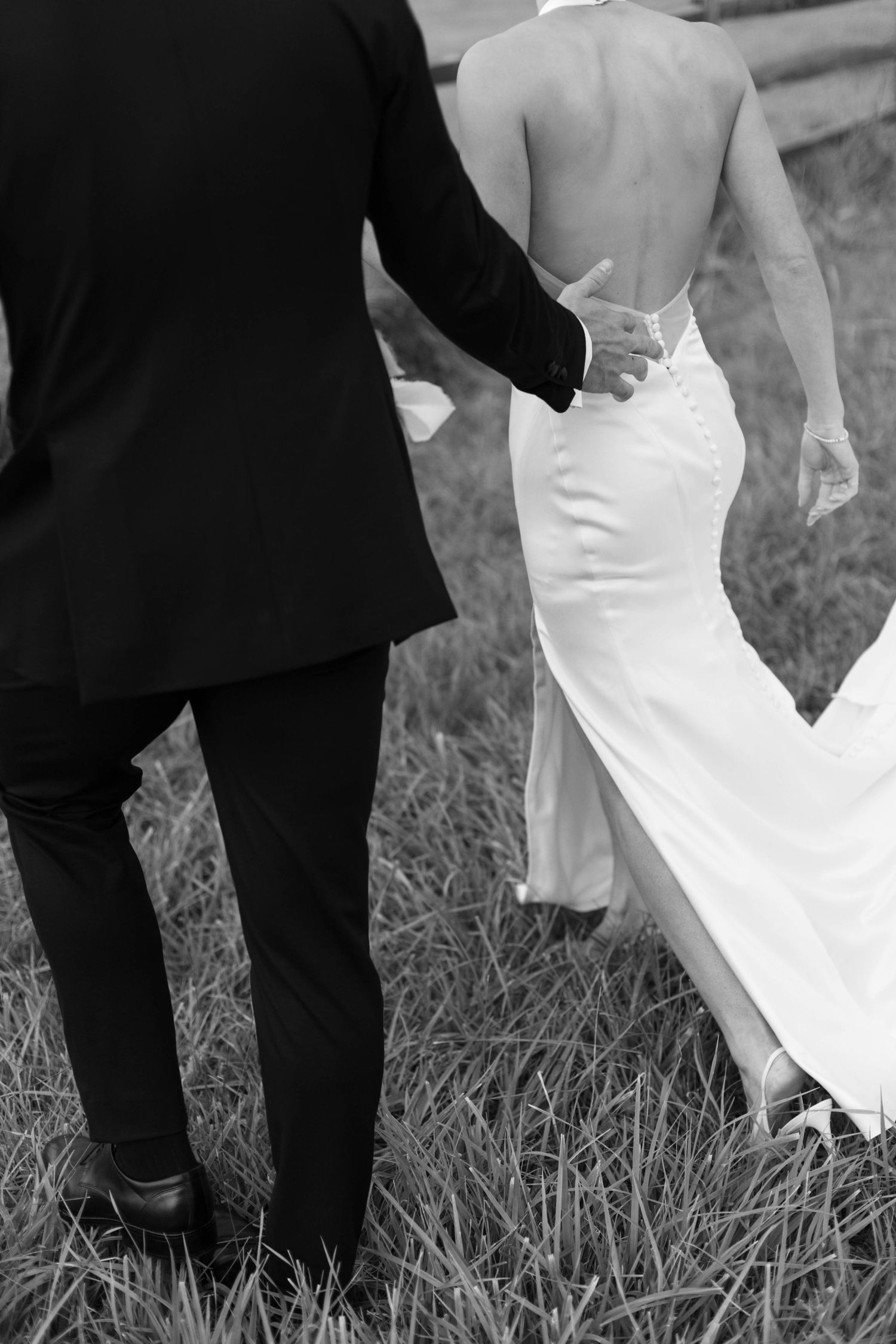 Black and white detail shot of couple walking through grass field.