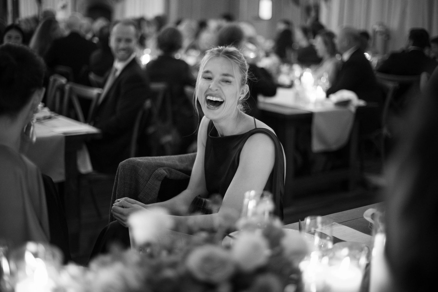 A candid black and white photo of a guest laughing joyfully at a formal dinner reception.