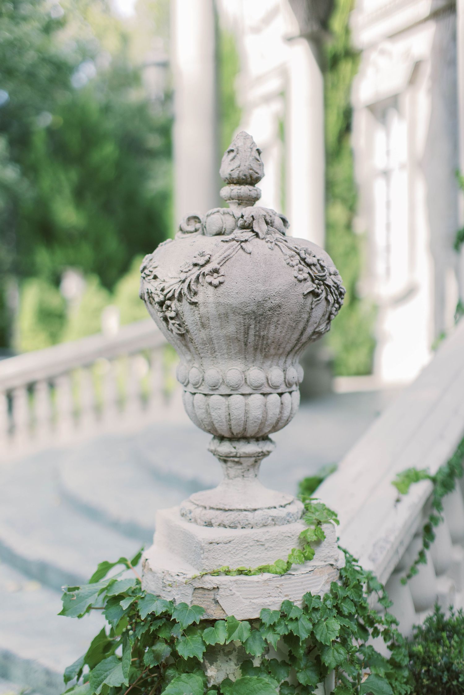 Ornate stone finial with decorative carvings and ivy growing at its base on an elegant porch balustrade.
