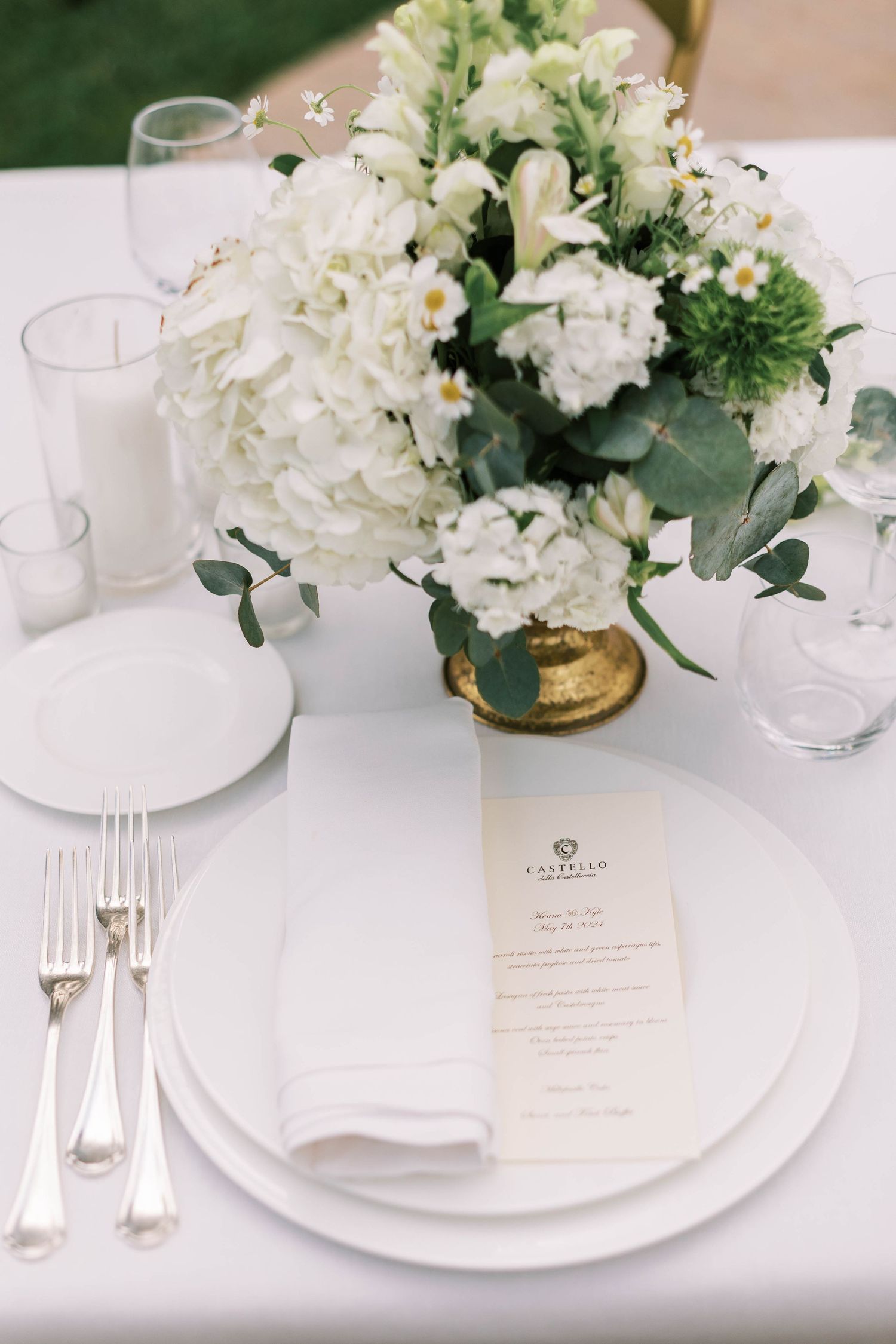 Elegant white floral centerpiece with eucalyptus on formal place setting with menu card.