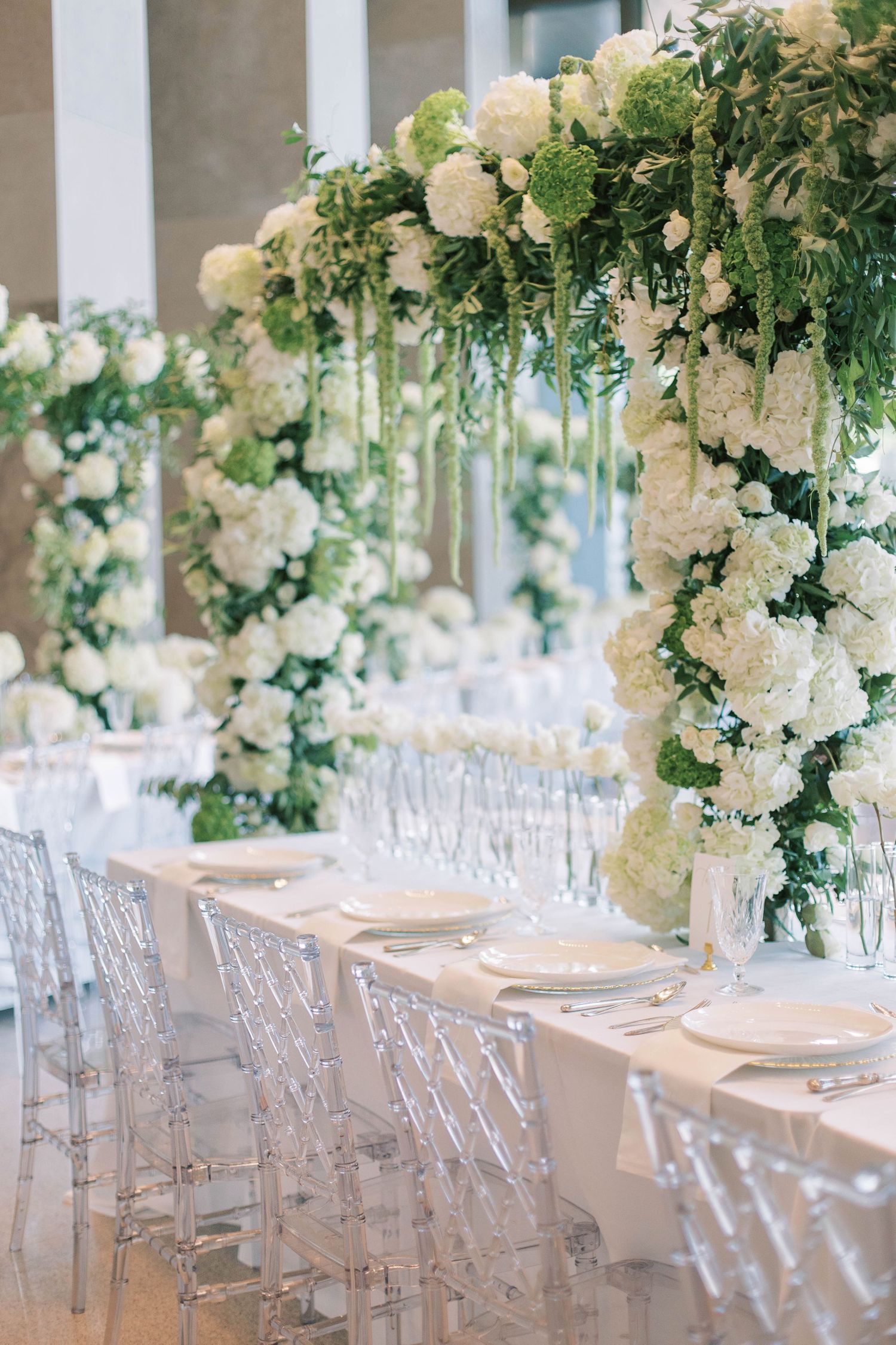Elegant wedding table setting with crystal chairs and lush white hydrangea arrangements.