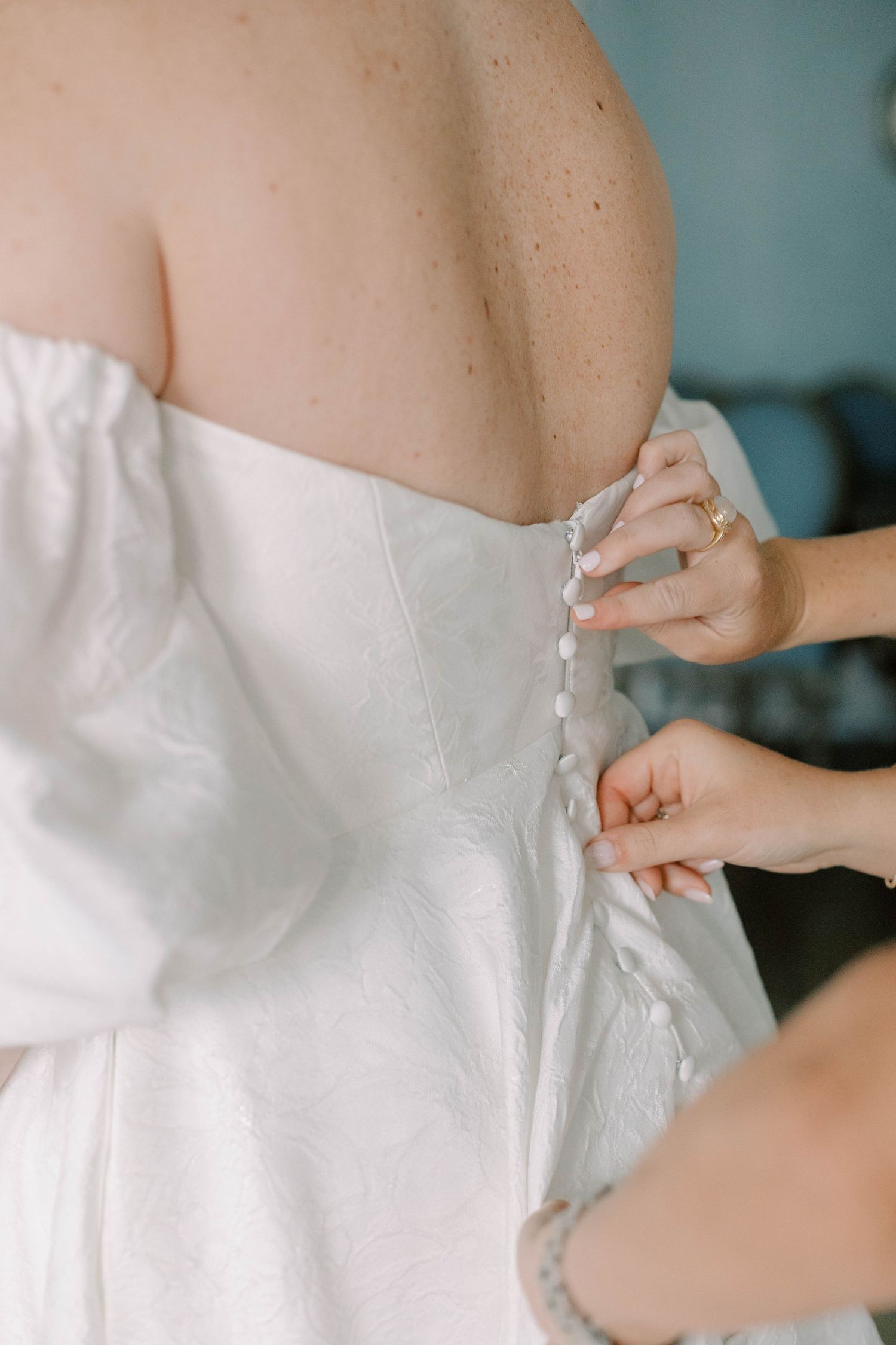 Close-up of hands buttoning up the back of a white wedding dress.