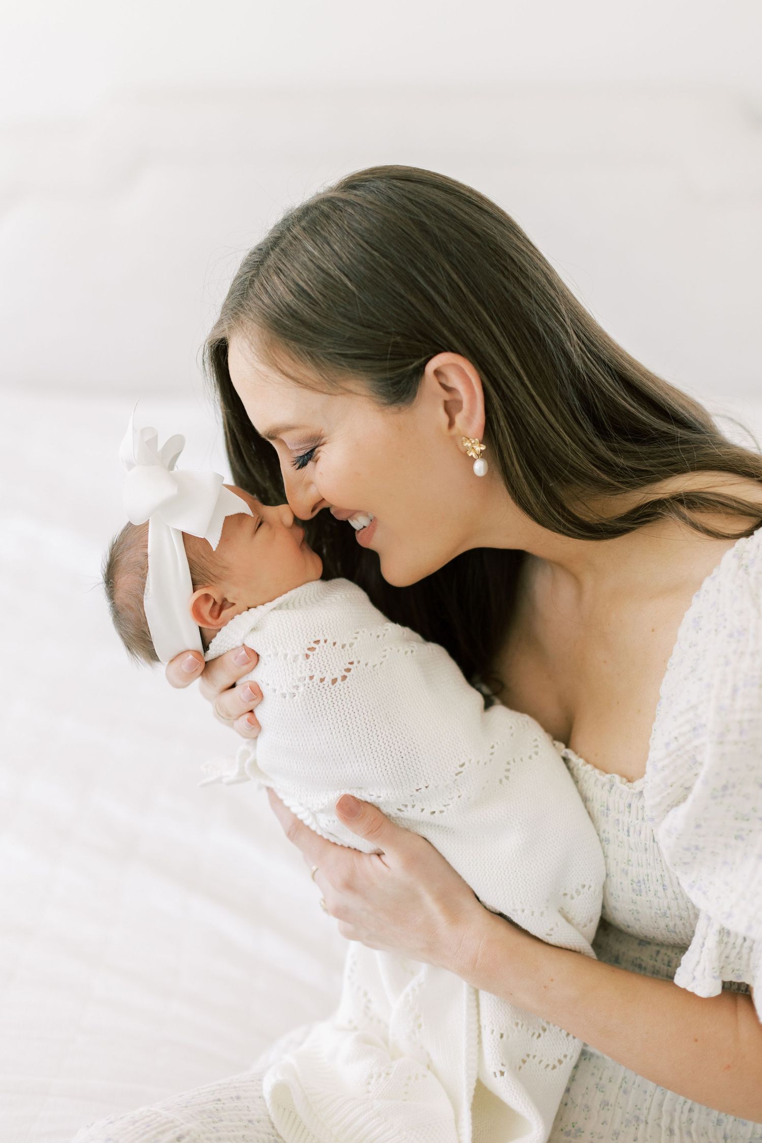 A tender moment between parent and newborn baby dressed in white lace against a light background.