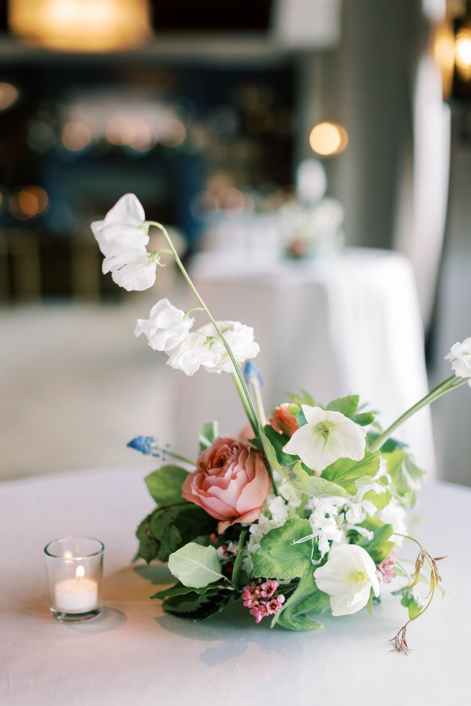 Delicate floral centerpiece with pink roses and white orchids on a white tablecloth.