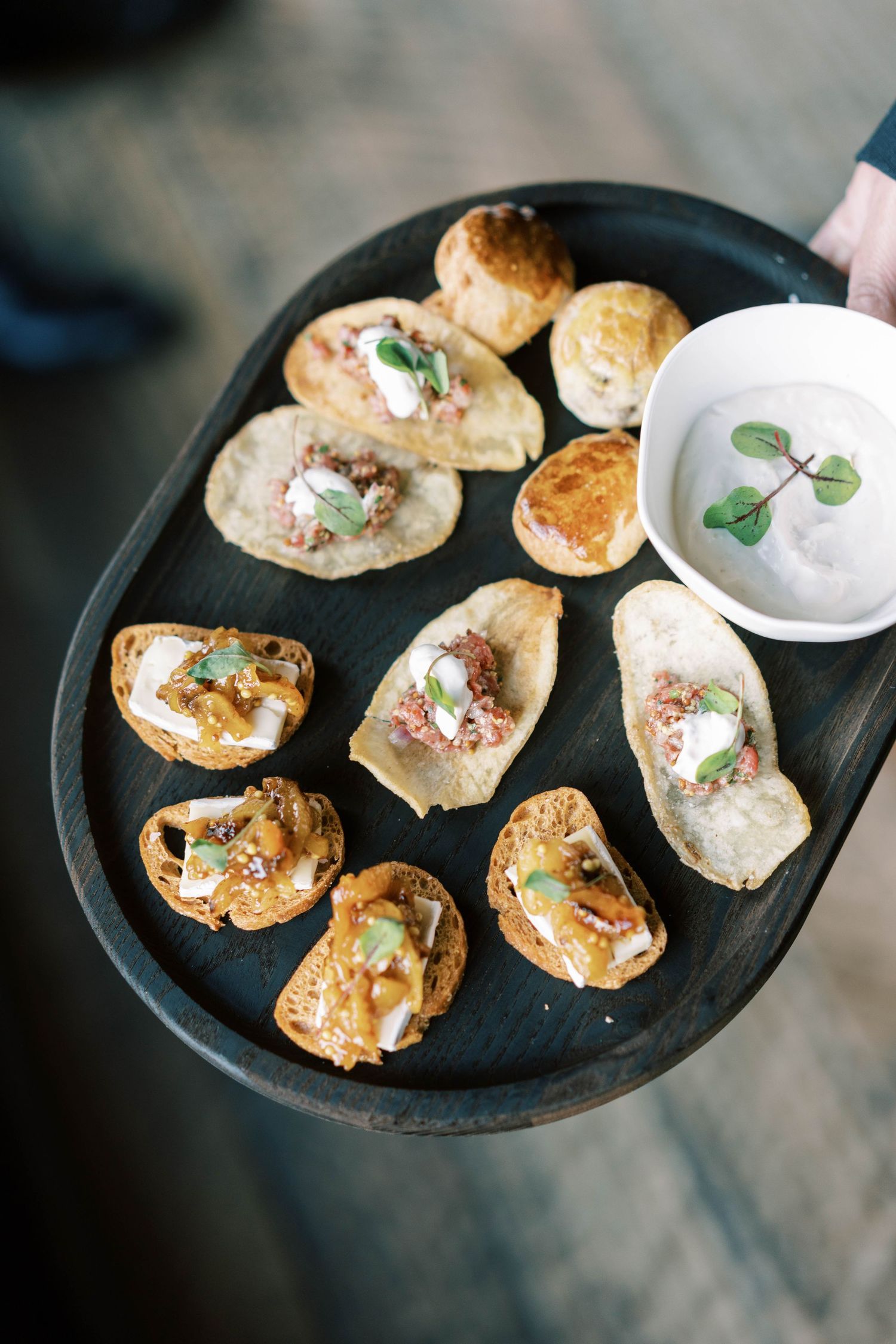 Artfully plated hors d'oeuvres on a black serving tray with a side of cream sauce.
