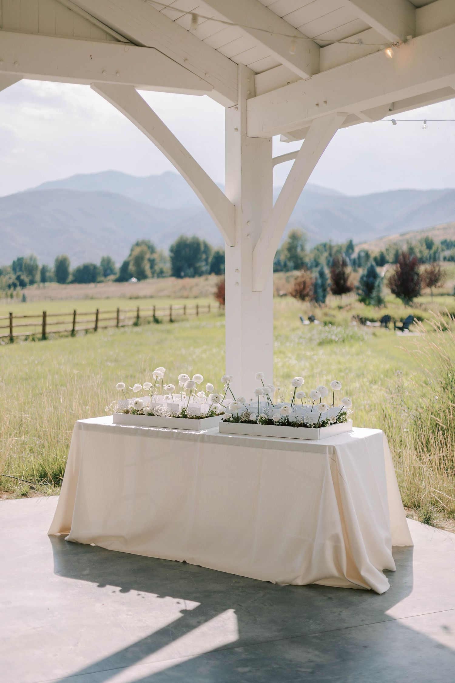 White-draped reception table with elegant decor under covered patio overlooking mountain landscape.