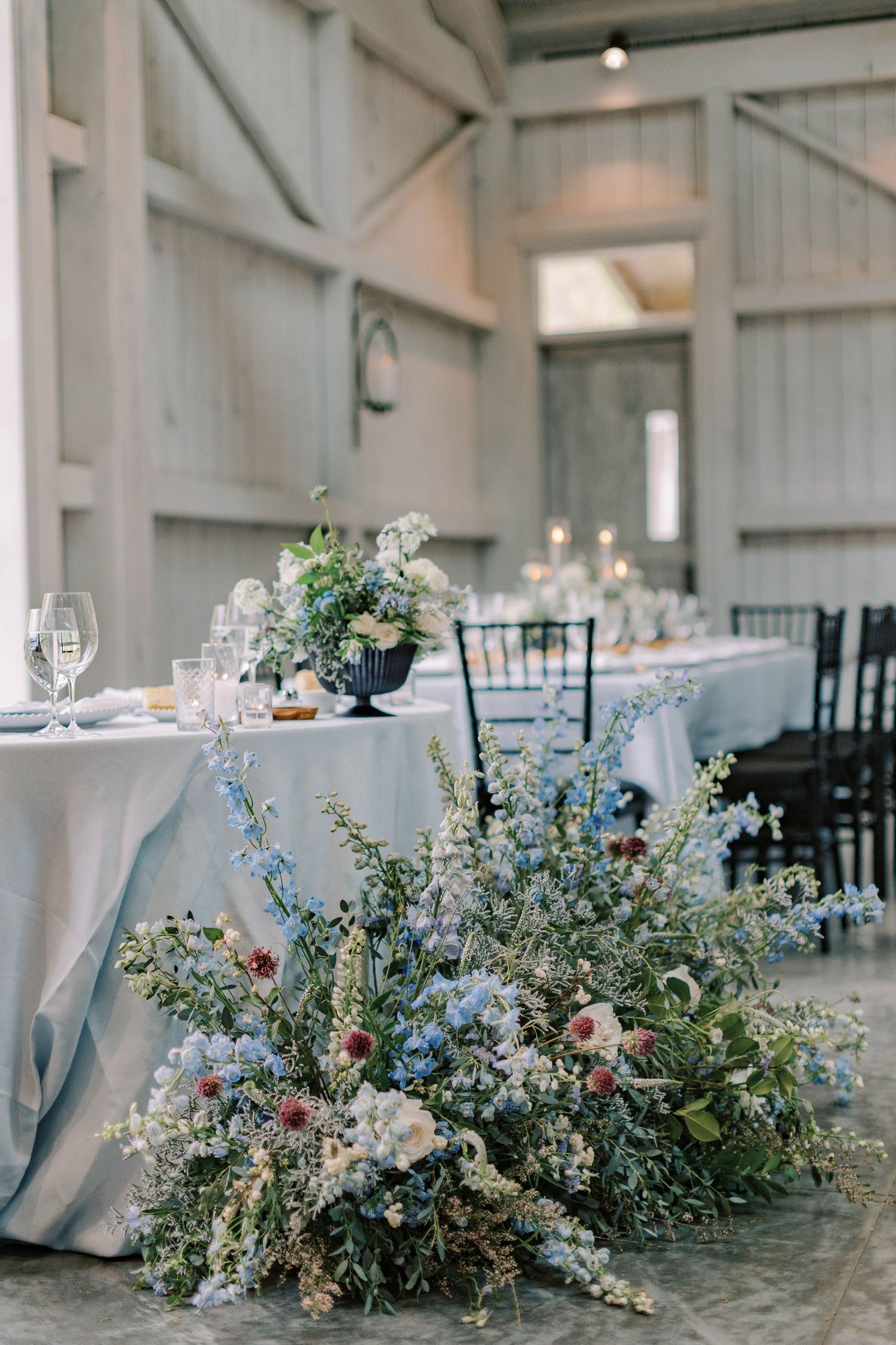 Rustic barn wedding reception setup with romantic floral arrangements and white tablecloths.