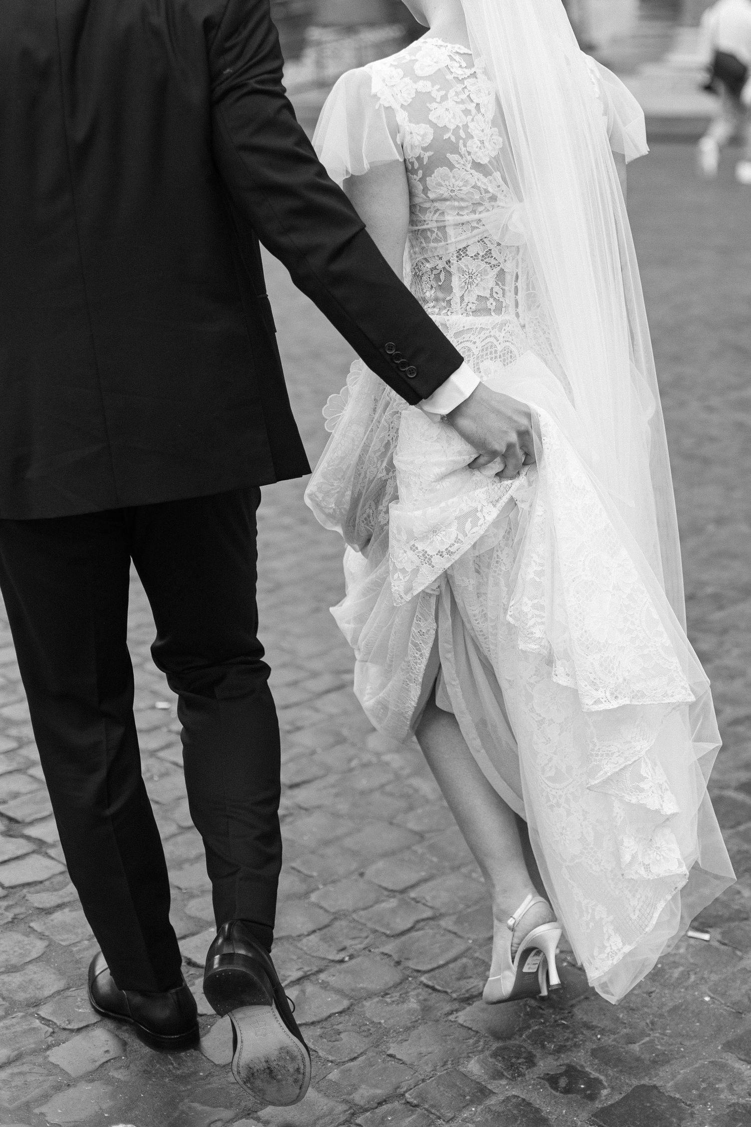 Black and white detail shot of bride and groom's legs with wedding dress train and formal shoes.