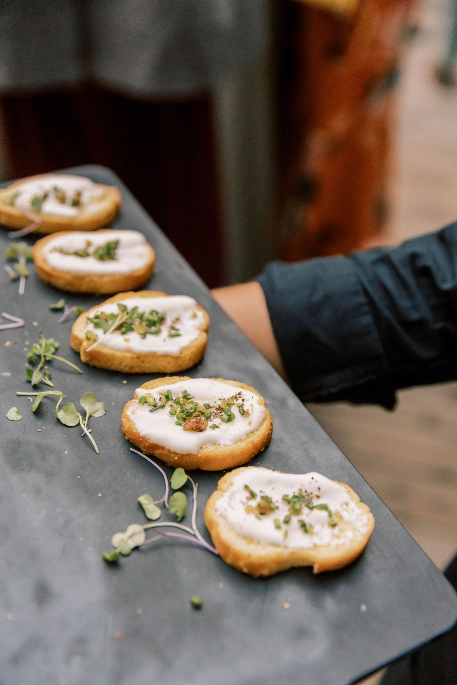 Artisanal crostini topped with cream and microgreens served on a slate board.