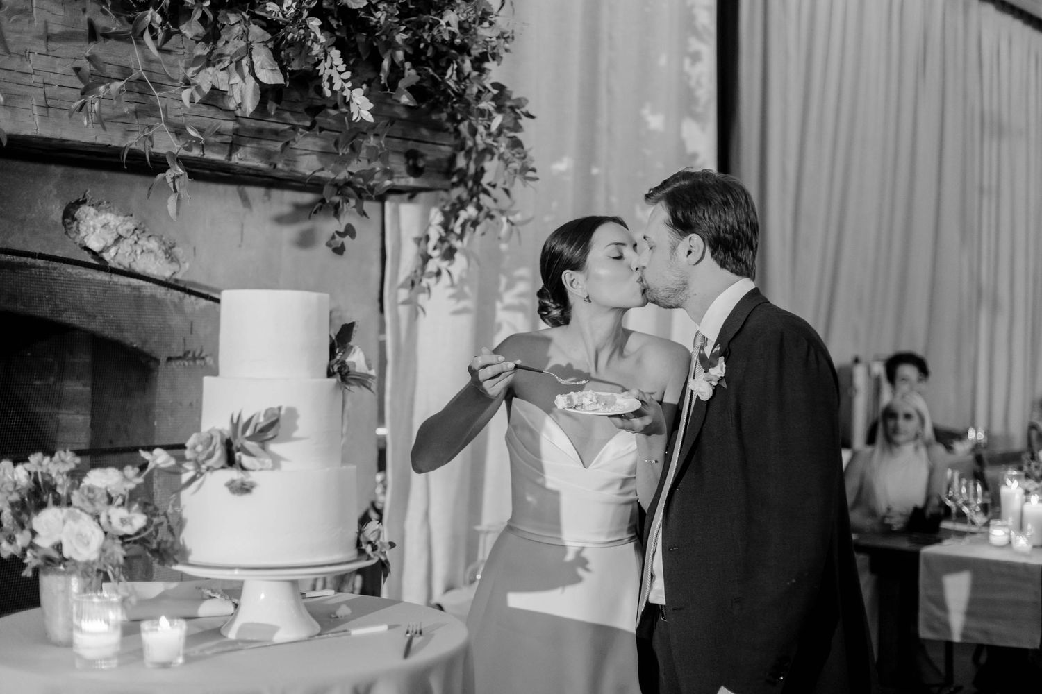 A couple shares a sweet moment while cutting their wedding cake at an elegant indoor reception.