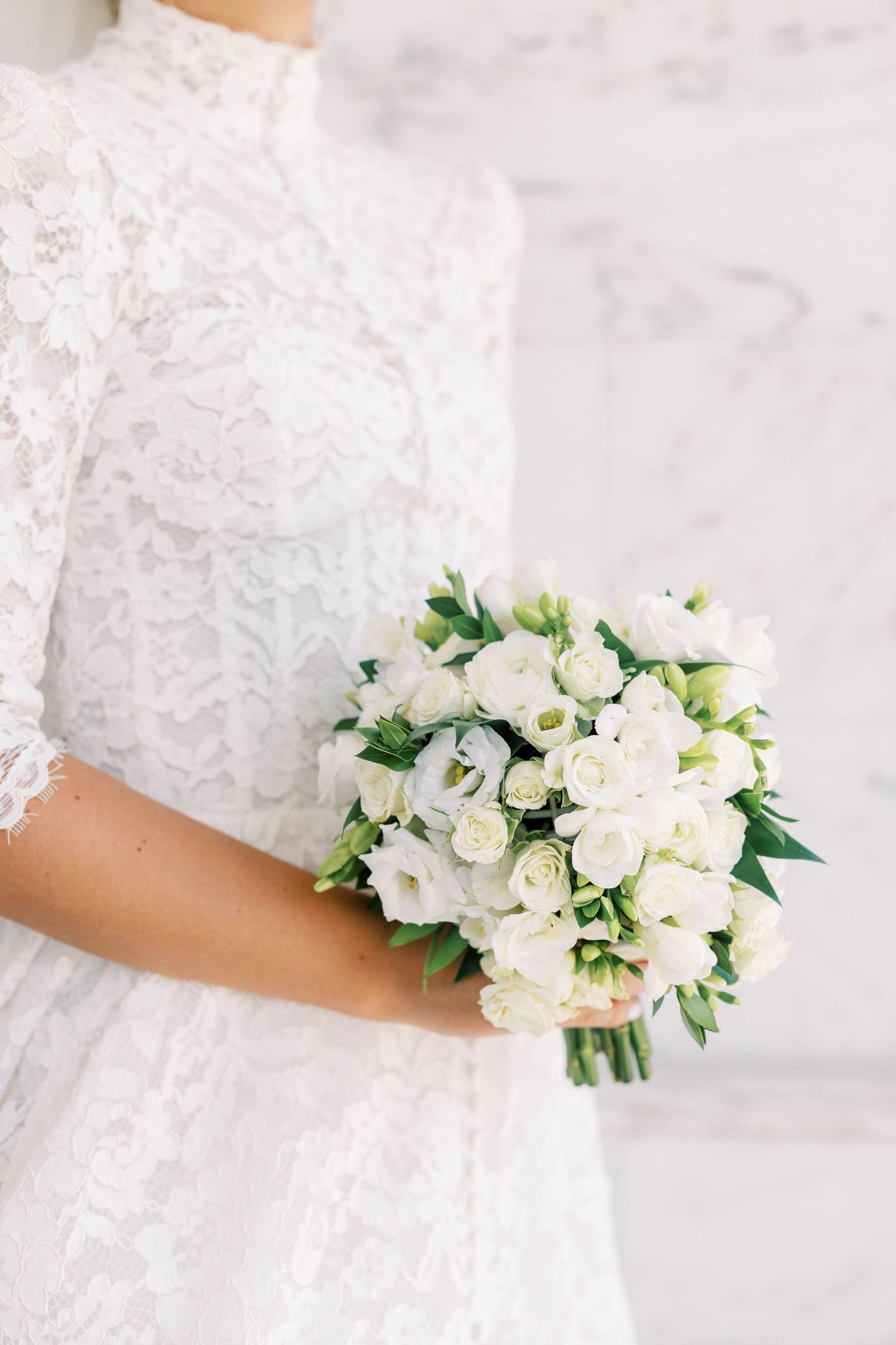 Elegant white bridal bouquet of roses held against a lace wedding dress.