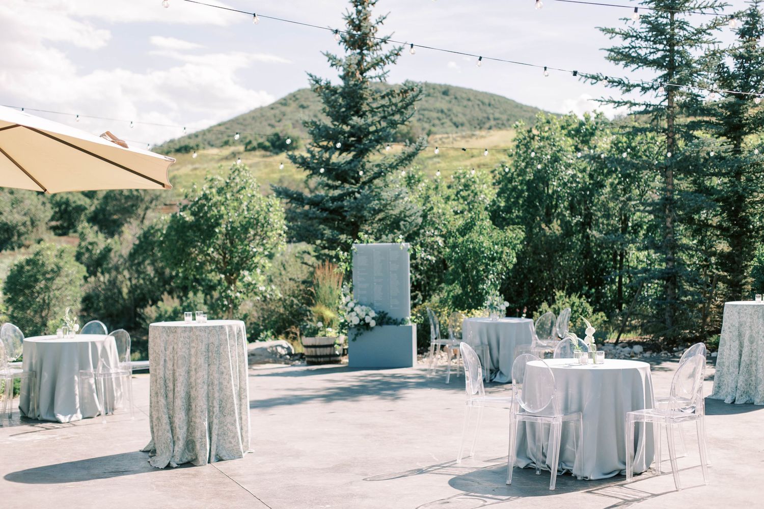 Outdoor wedding reception setup with white linen tables and mountain landscape backdrop.