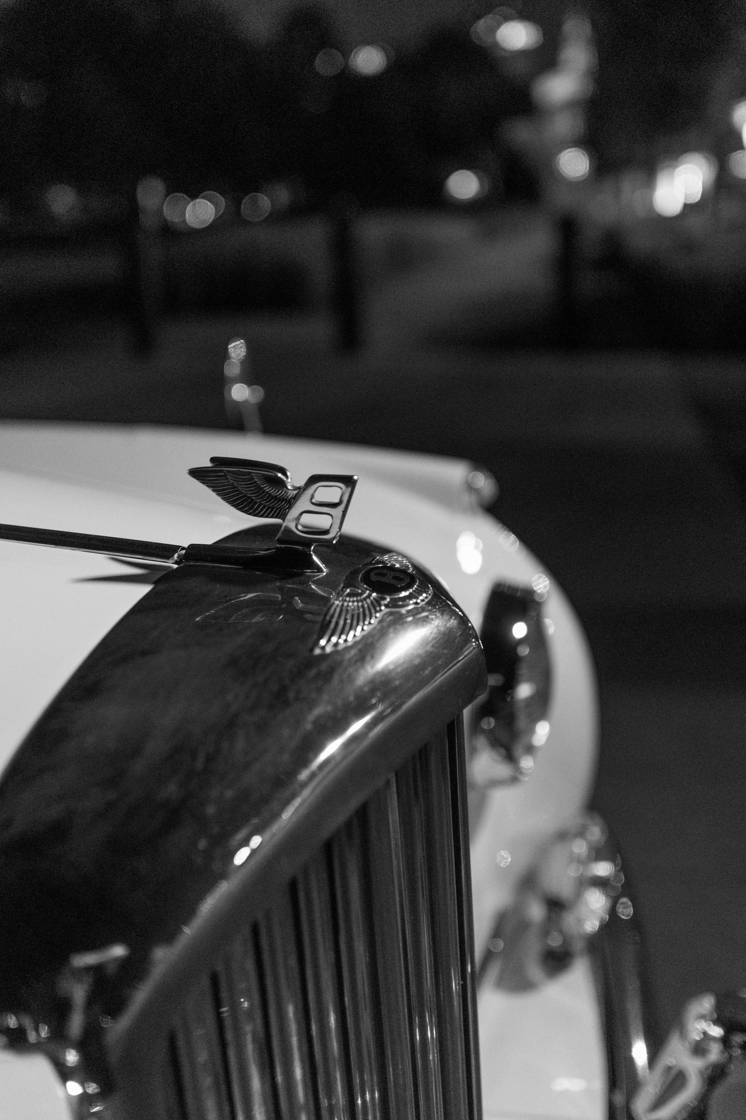 Close-up black and white photo of classic car hood ornament at night.