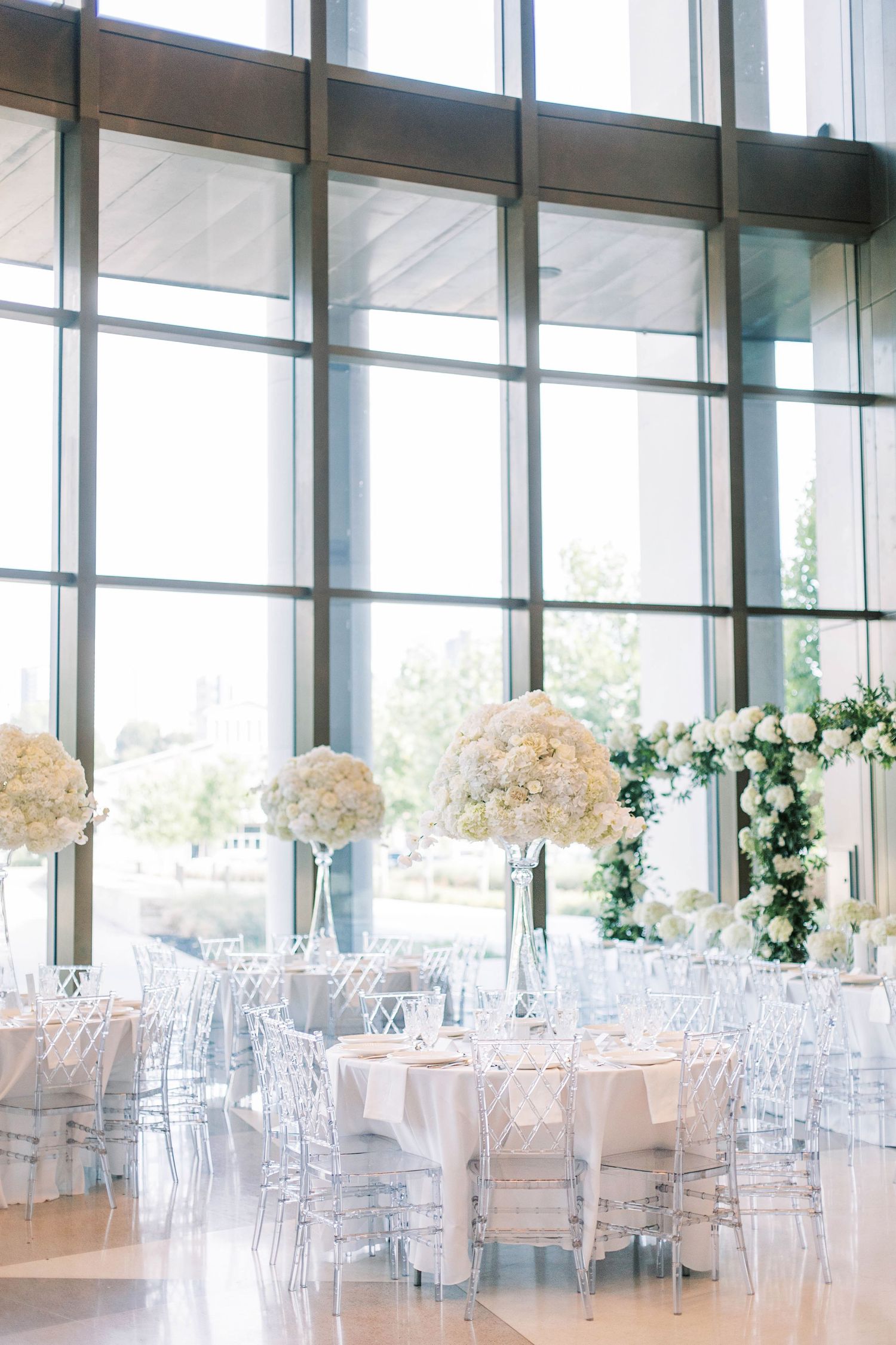 Modern reception venue with floor-to-ceiling windows and white floral centerpieces.