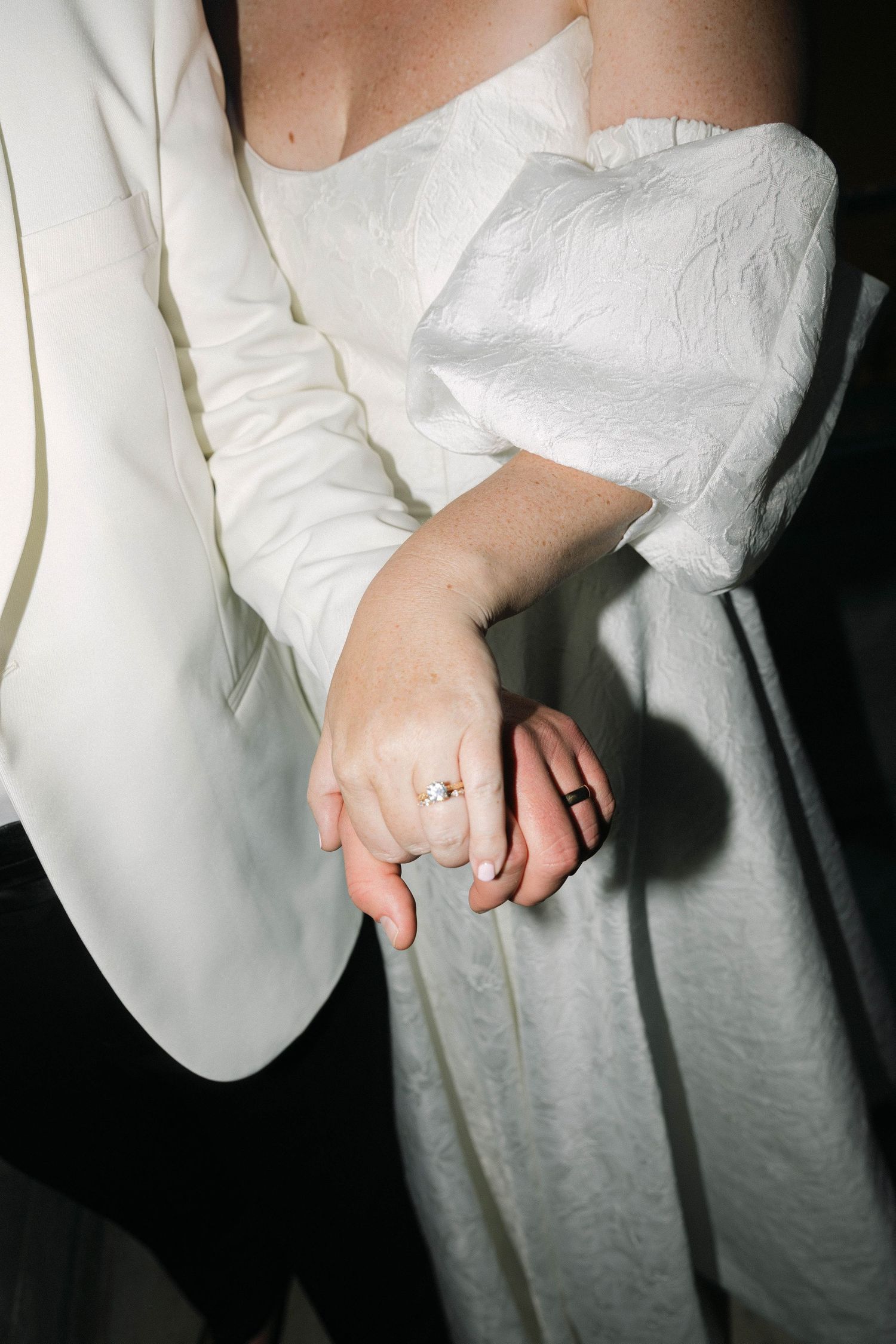 Close-up of elegant engagement ring on bride's hand against white wedding attire.