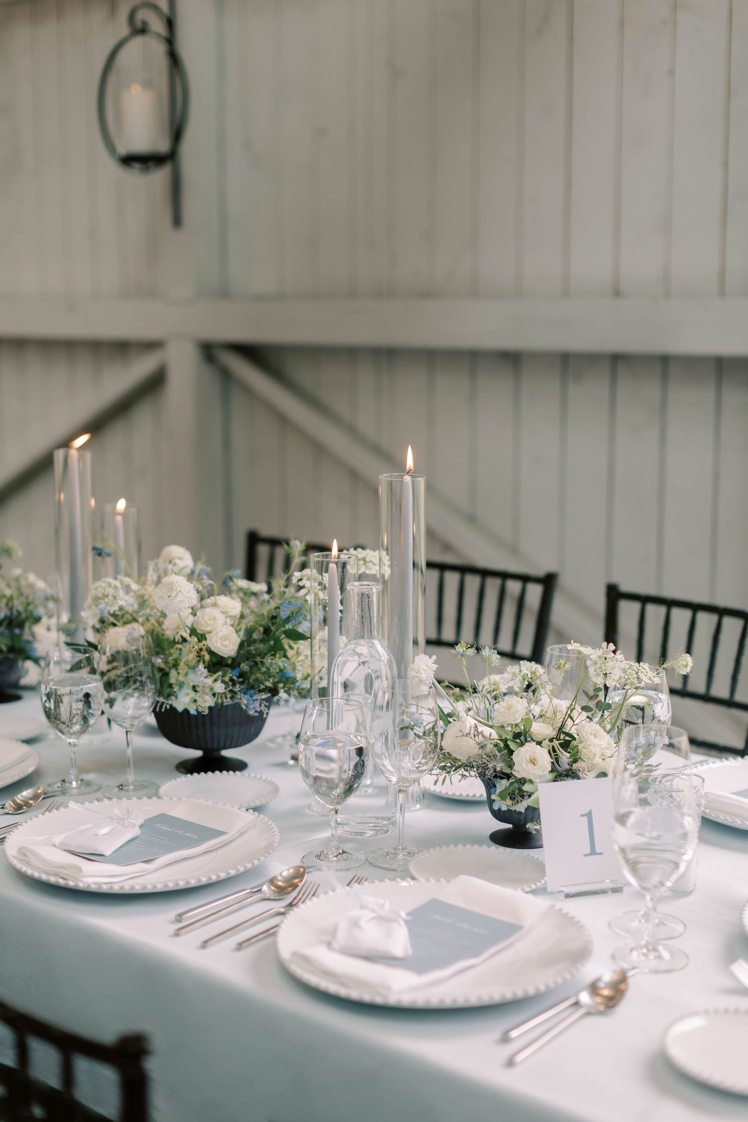 Wedding table setting with white linens, taper candles, and blue floral centerpieces.