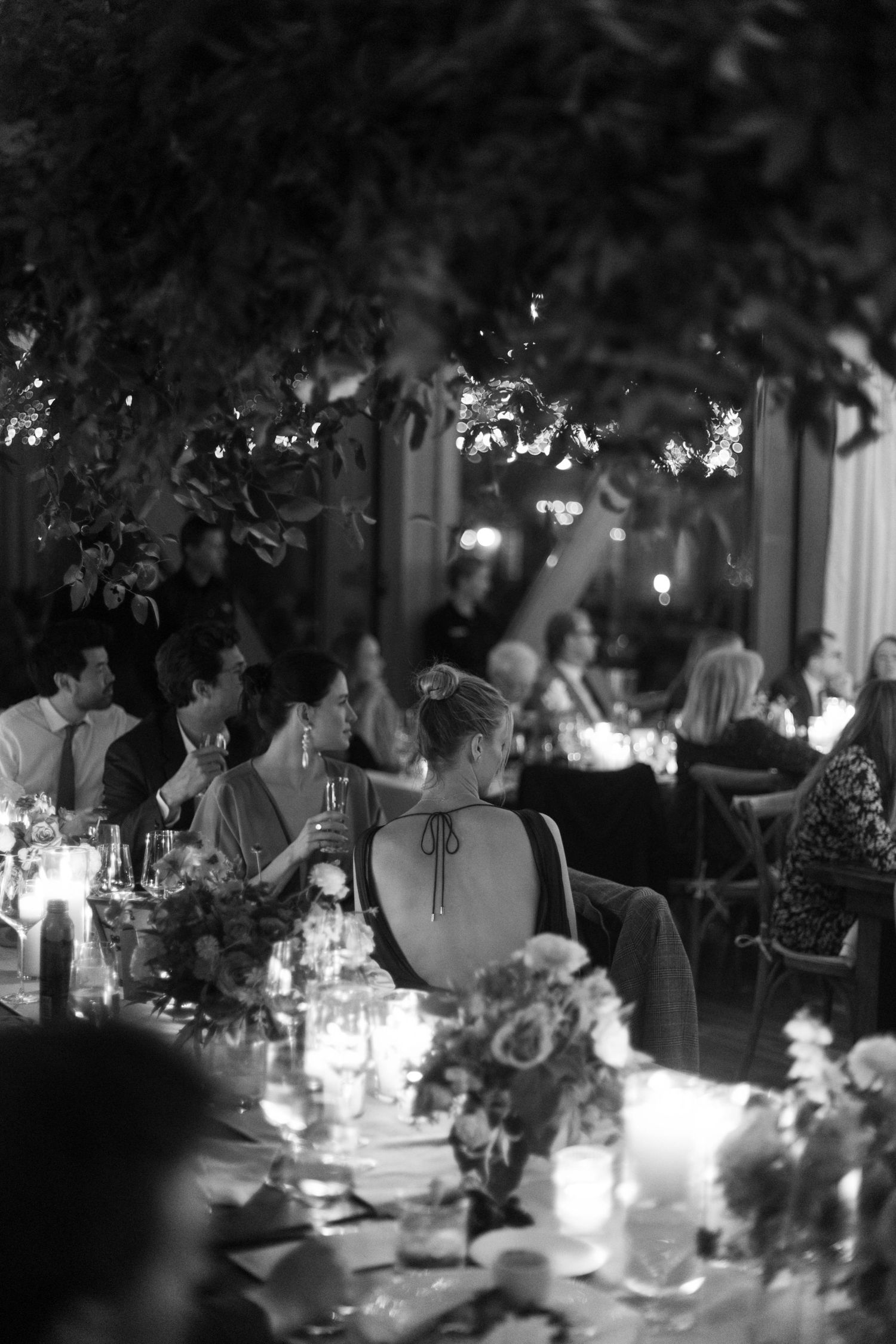 Black and white photo of an intimate dinner party with candlelight and floral table decorations.