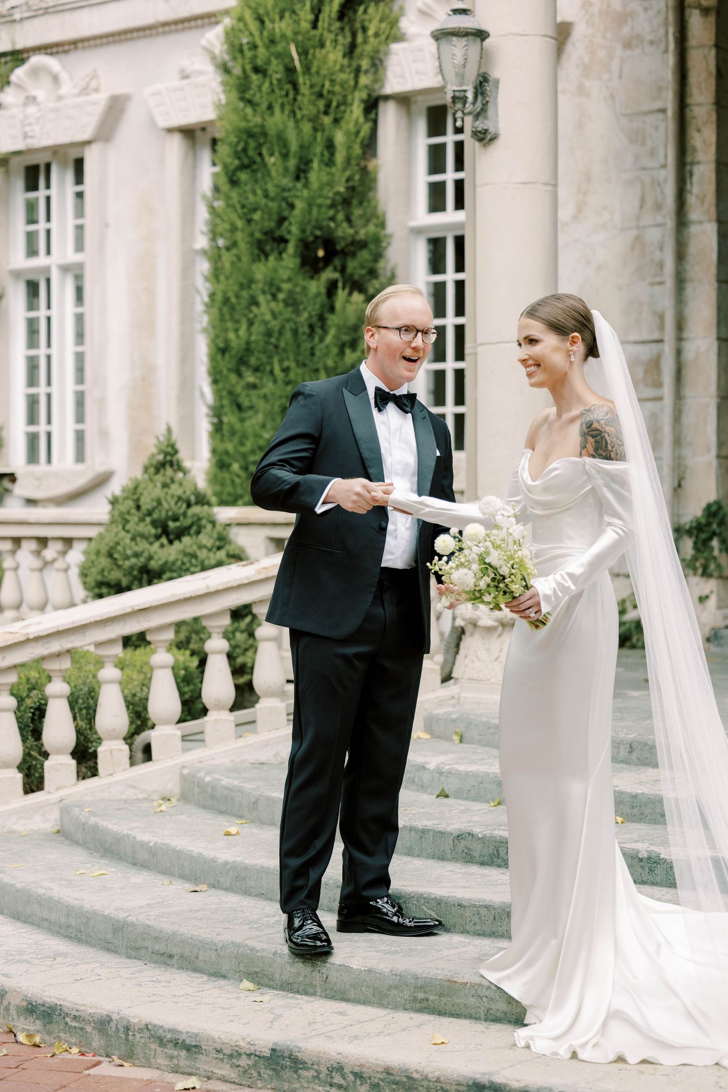 Wedding couple standing on stone steps of grand mansion.