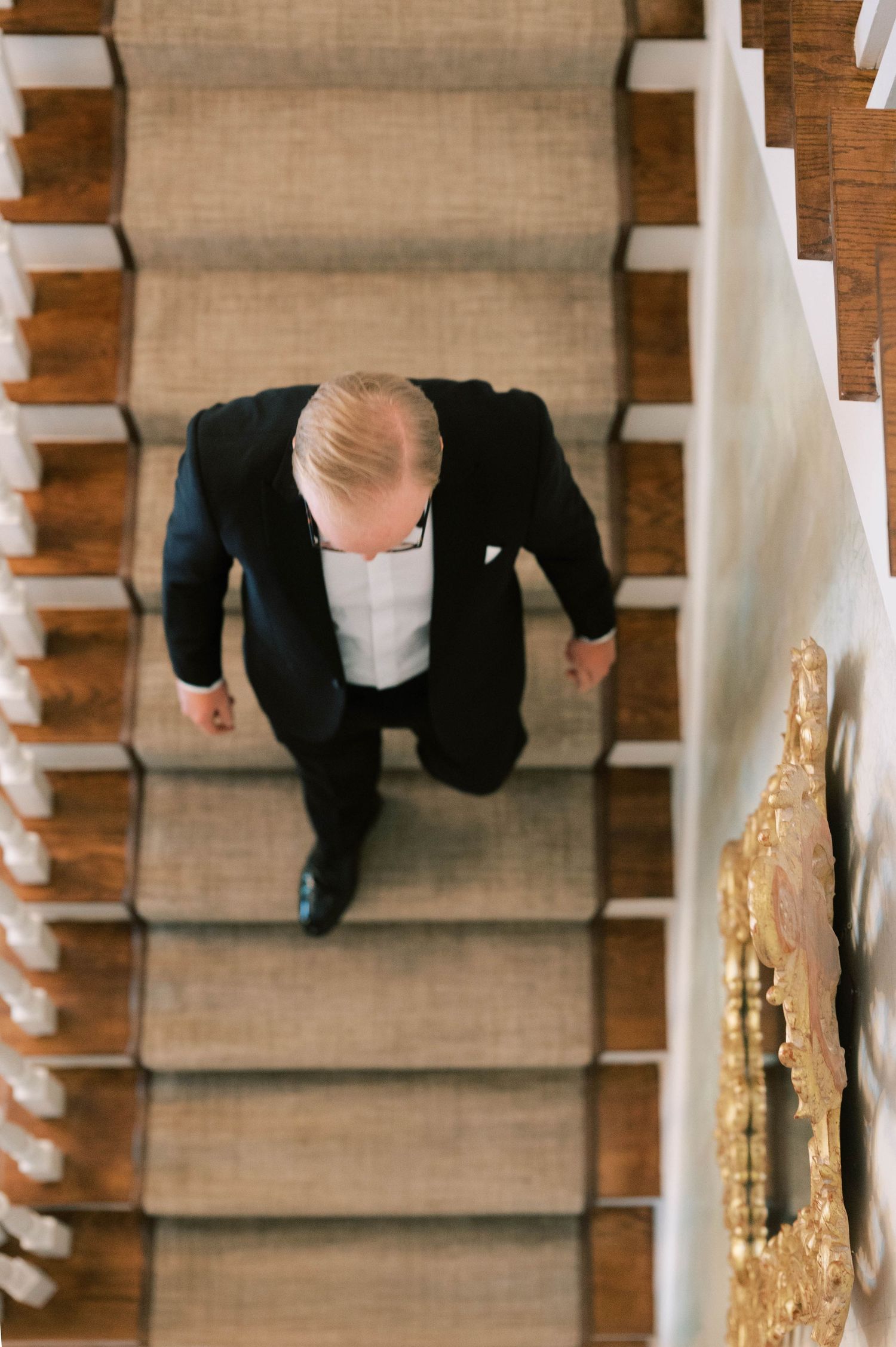 Bird's eye view of formal attire ascending carpeted staircase in traditional interior.
