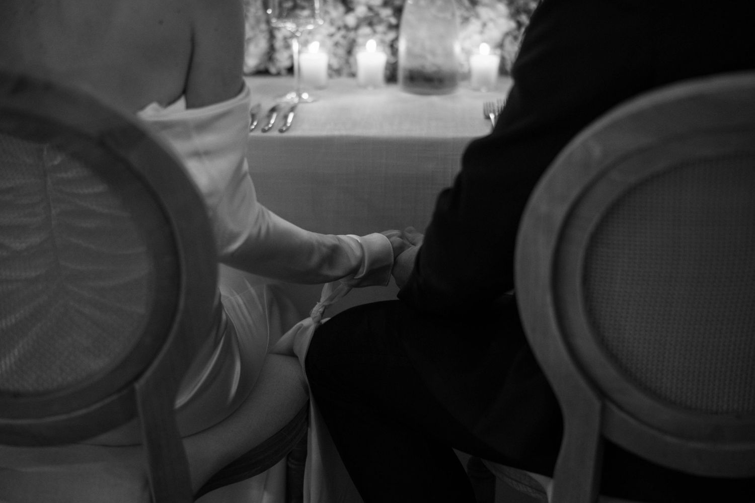 Black and white image of guests seated at an intimate dinner setting with ornate chairs.