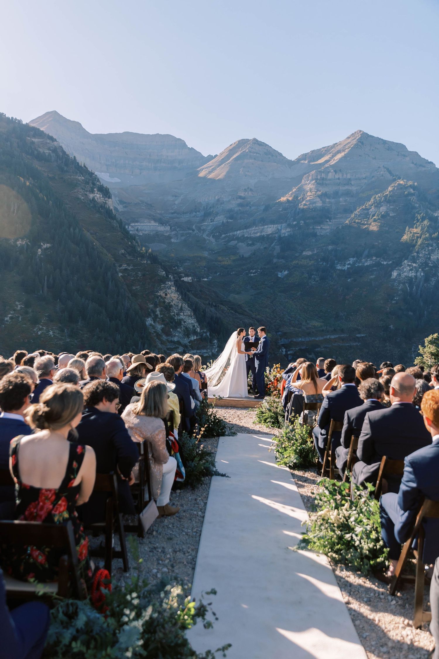Outdoor mountain wedding ceremony with seated guests and dramatic peaks in background.