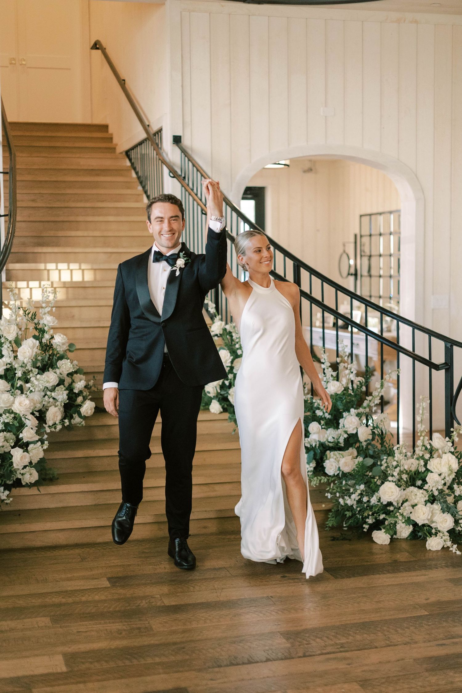 A couple descending elegant stairs decorated with white floral arrangements at their wedding.