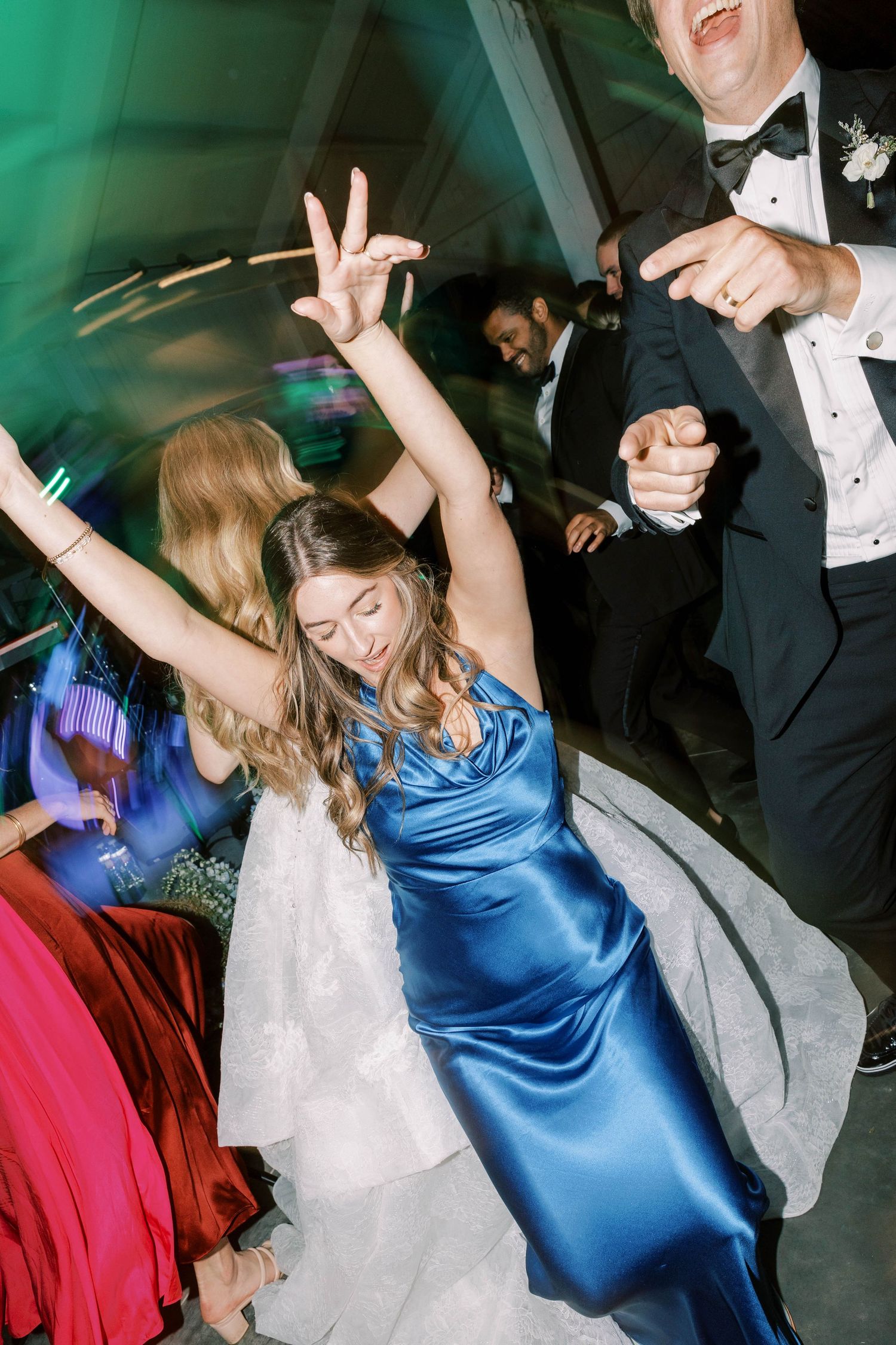 Wedding guests dancing energetically on the reception dance floor with colorful lighting.