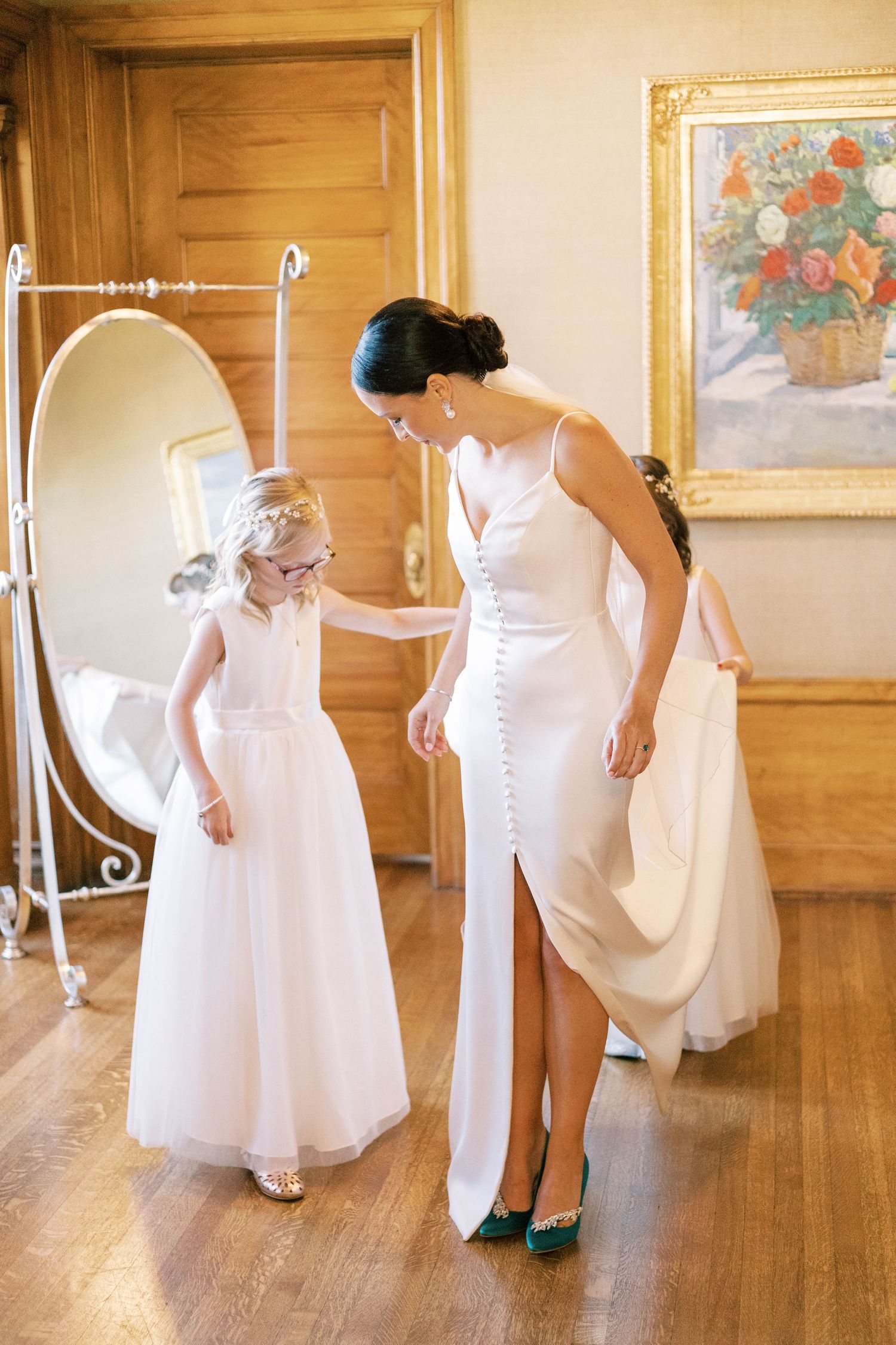 Bride in white dress showing matching flower girl her elegant teal heels.