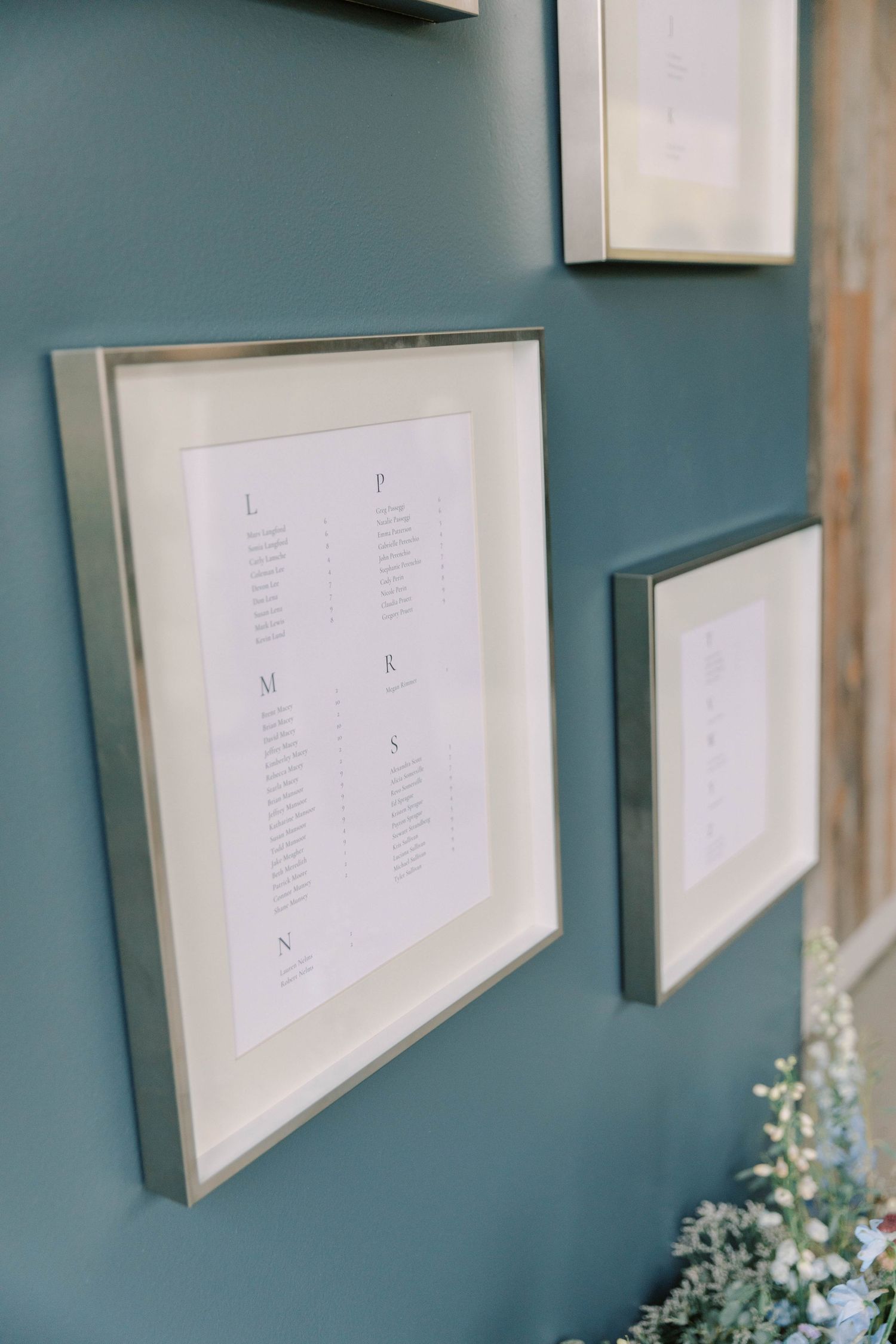 Close-up of elegant wedding seating chart frames mounted on teal-colored wall.