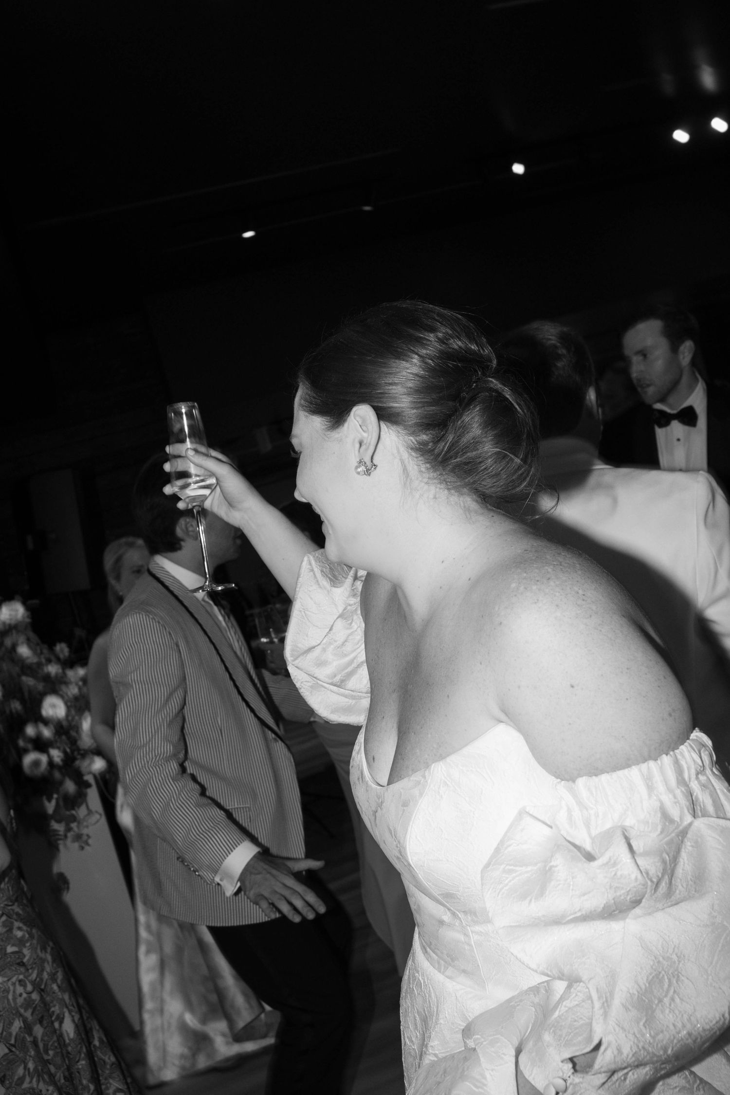 Wedding guest in formal attire raising a champagne glass at an elegant evening reception.