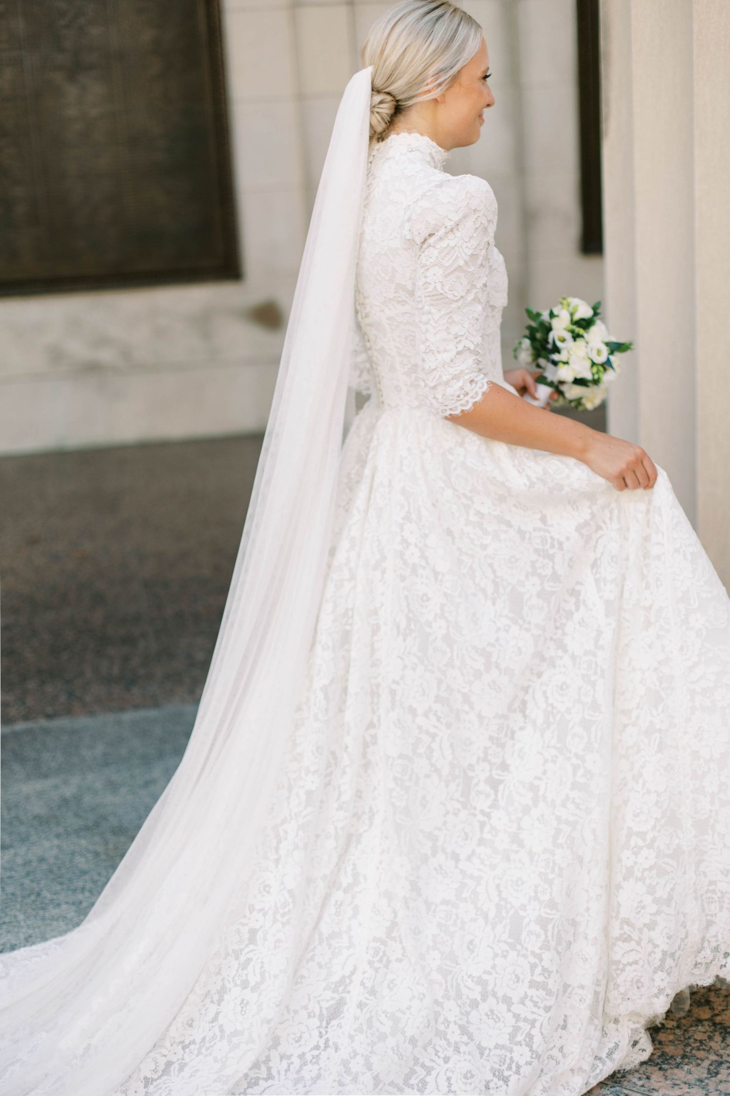Elegant lace wedding dress with long sleeves and flowing veil captured in a classic side profile pose.