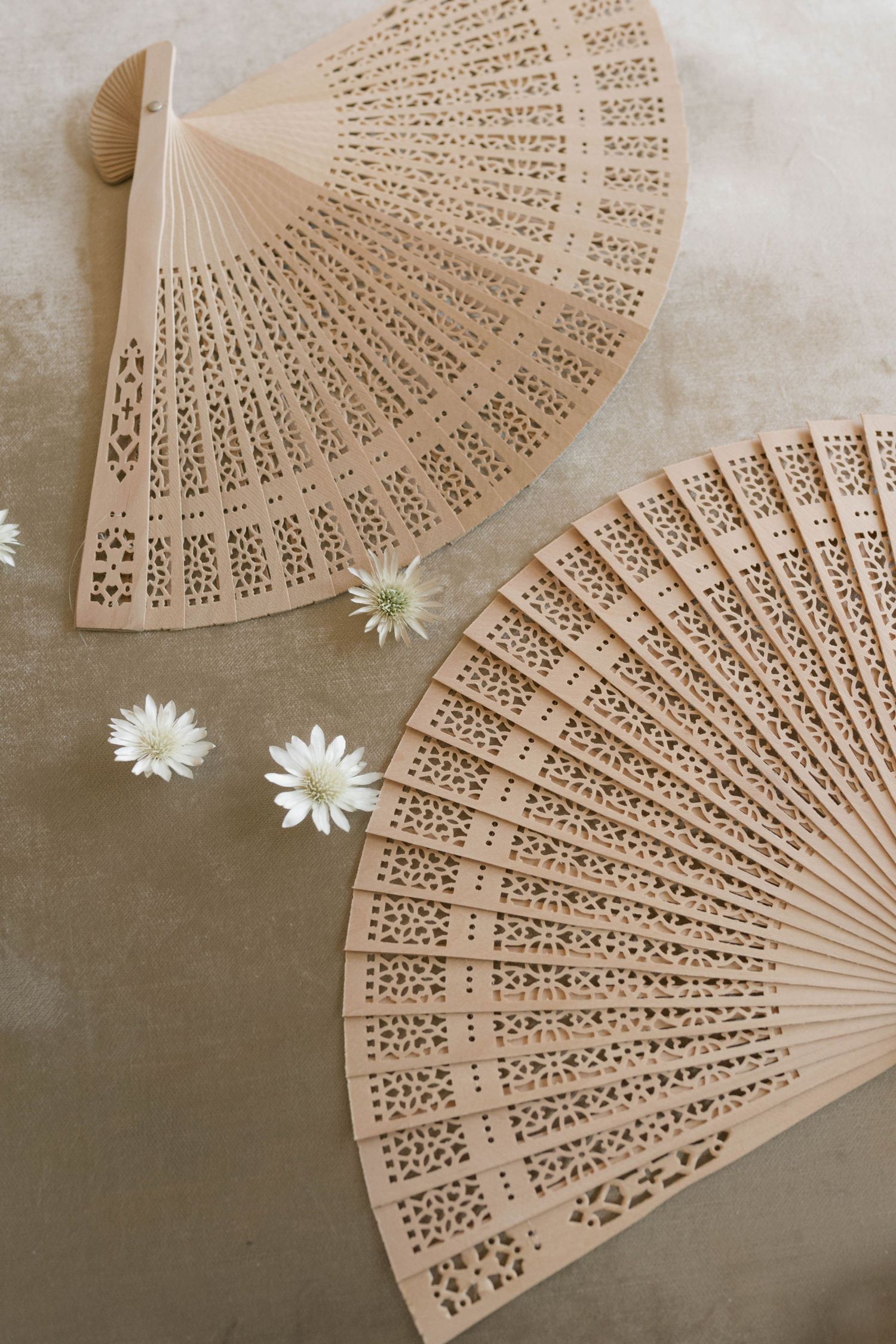 Two decorative wooden fans with intricate cutout patterns and white daisies.