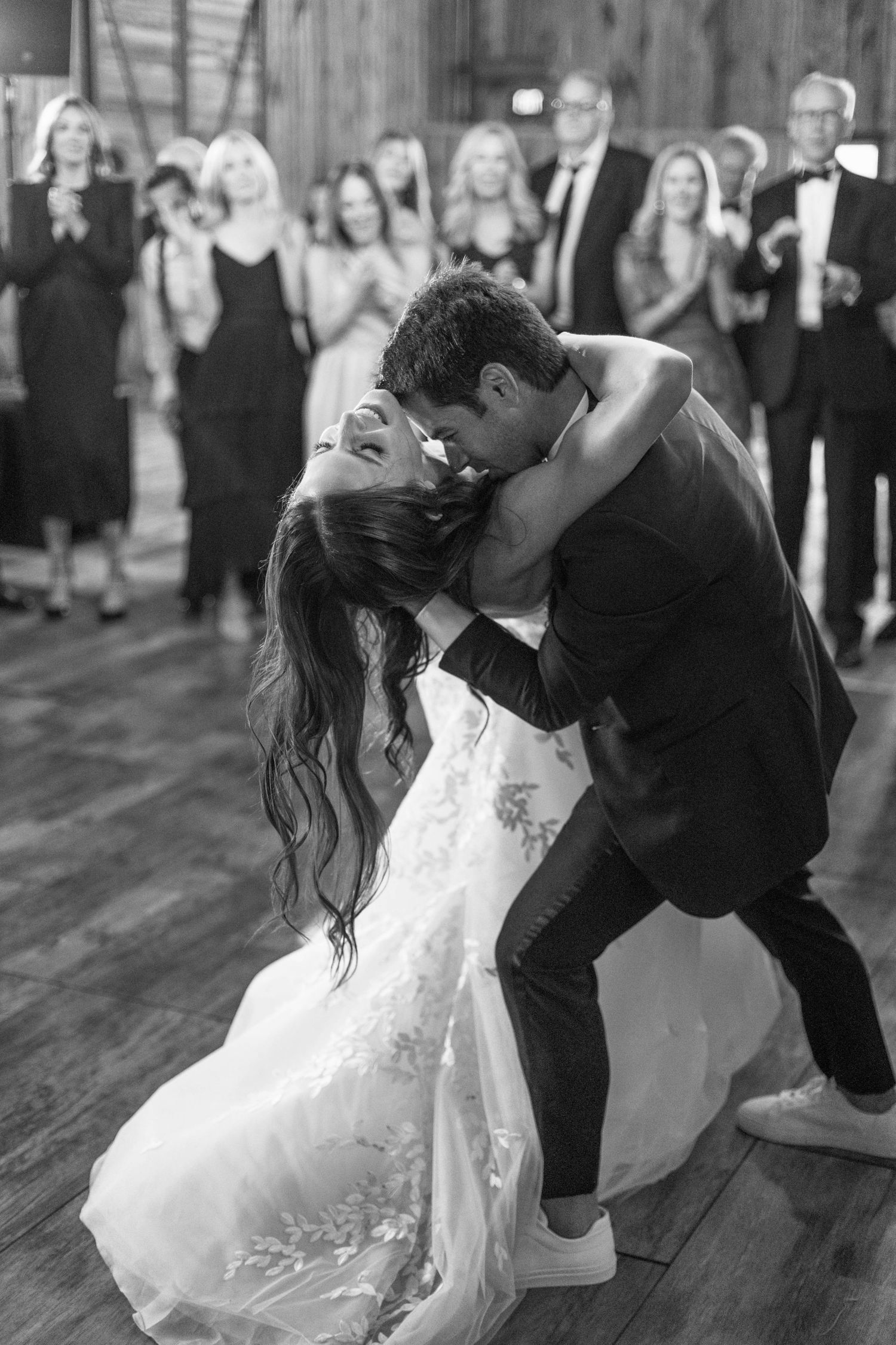 Romantic dance dip moment captured during wedding reception with guests looking on.