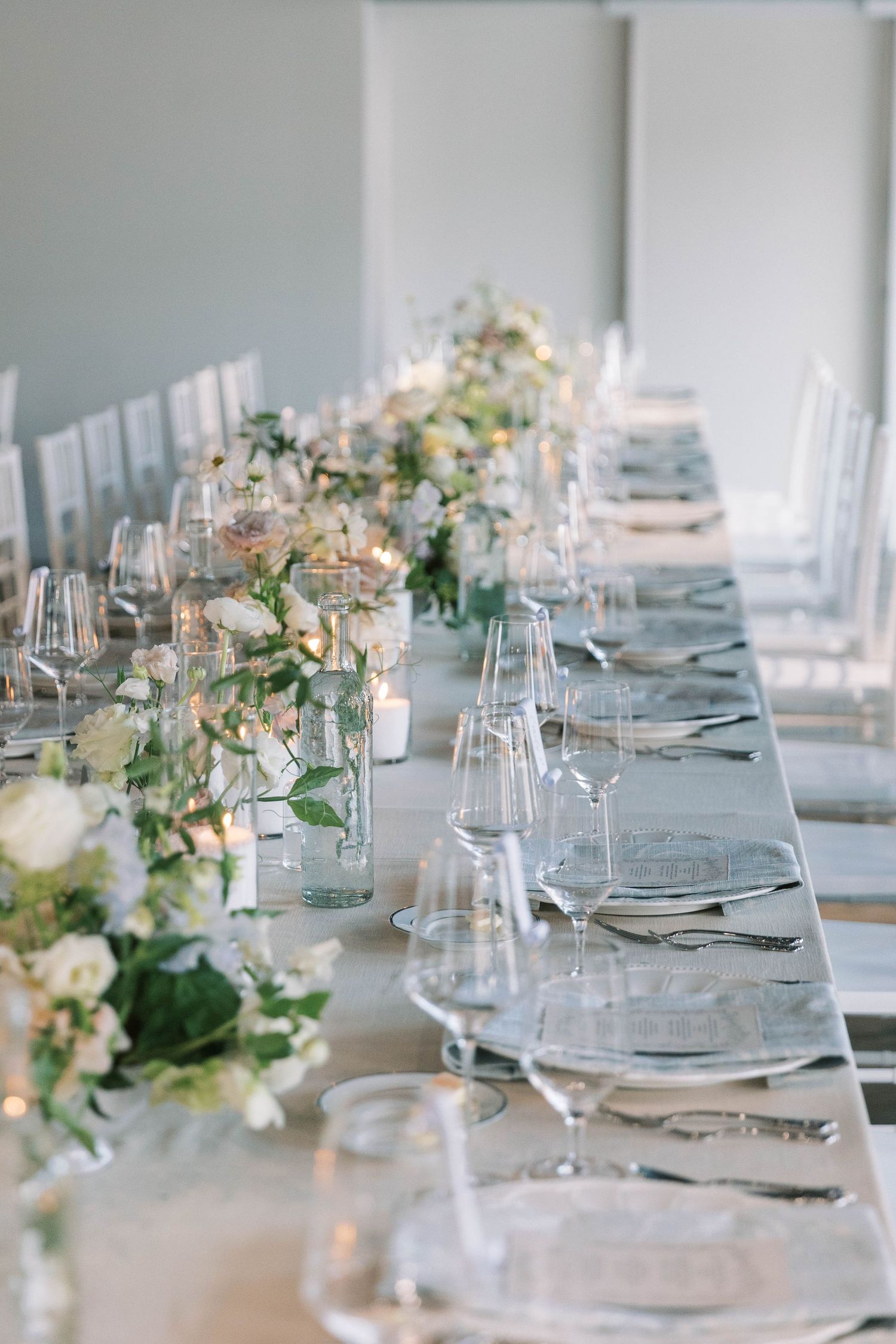 Long wedding reception table with white floral centerpieces and crystal place settings.