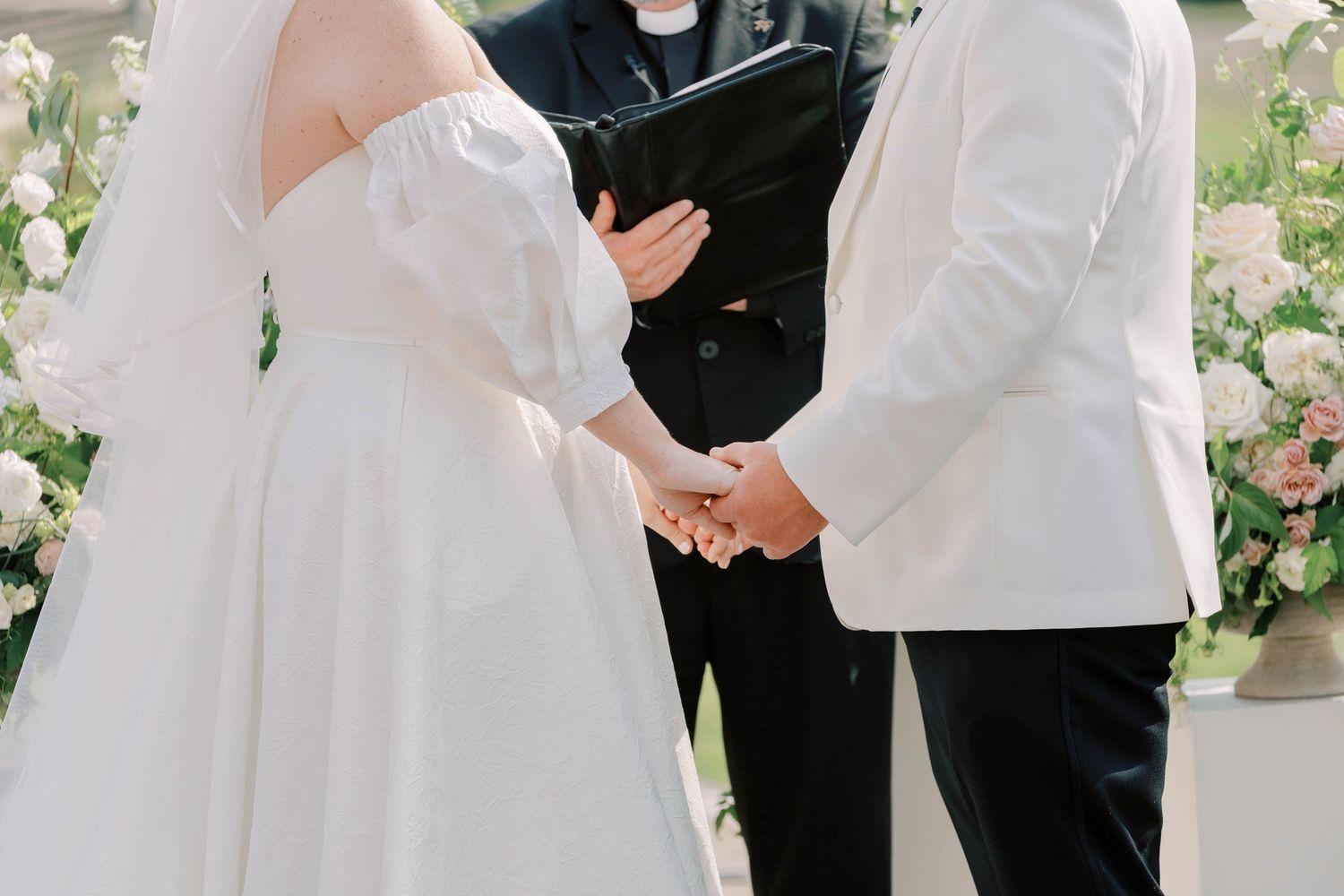 Close-up of couple holding hands during outdoor wedding ceremony.